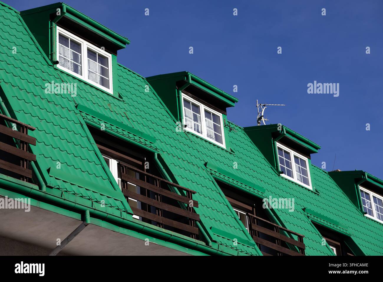 Prima piano di un tetto ondulato verde vivace con finestre a lucernario bianche e balconi in legno scuro, rappresentanti la costruzione residenziale e Foto Stock