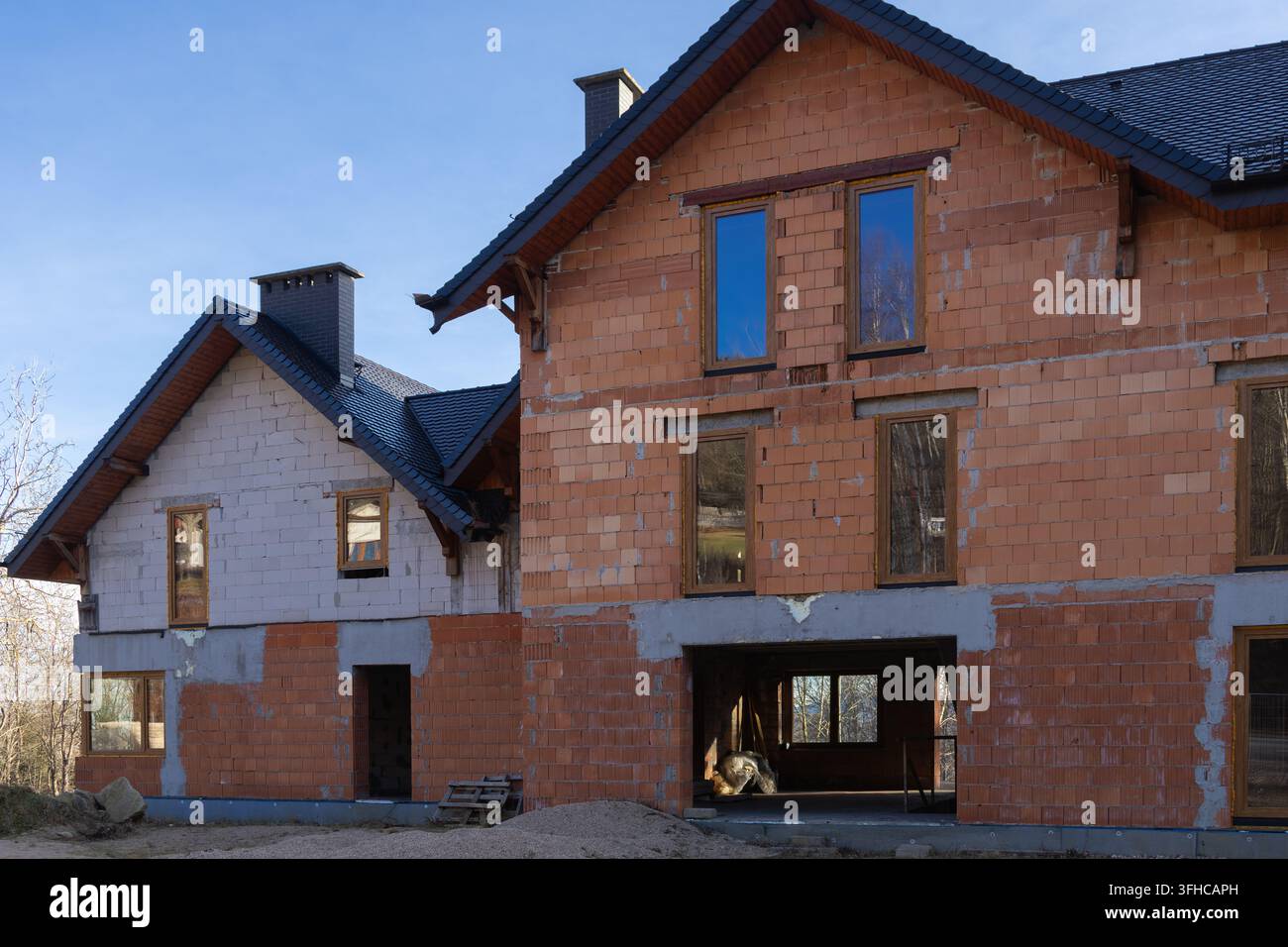 Panoramica di due proprietà residenziali moderne in costruzione, con pareti e tetti parzialmente completati contro un cielo blu chiaro, symboli Foto Stock