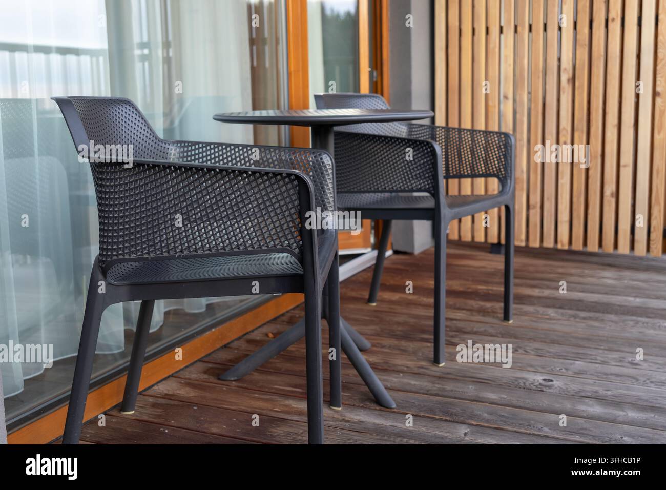 Primo piano di una moderna sistemazione da patio esterno con due sedie in rete nera e un tavolo, ideale per un balcone di hotel o un terrazzo di casa per un tranquillo tempo libero Foto Stock