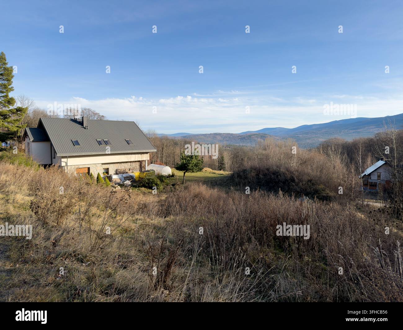 Vista elevata di una casa contemporanea con tetto grigio e facciata di colore chiaro, incastonata in un paesaggio autunnale arido, che rappresenta una contea tranquilla Foto Stock