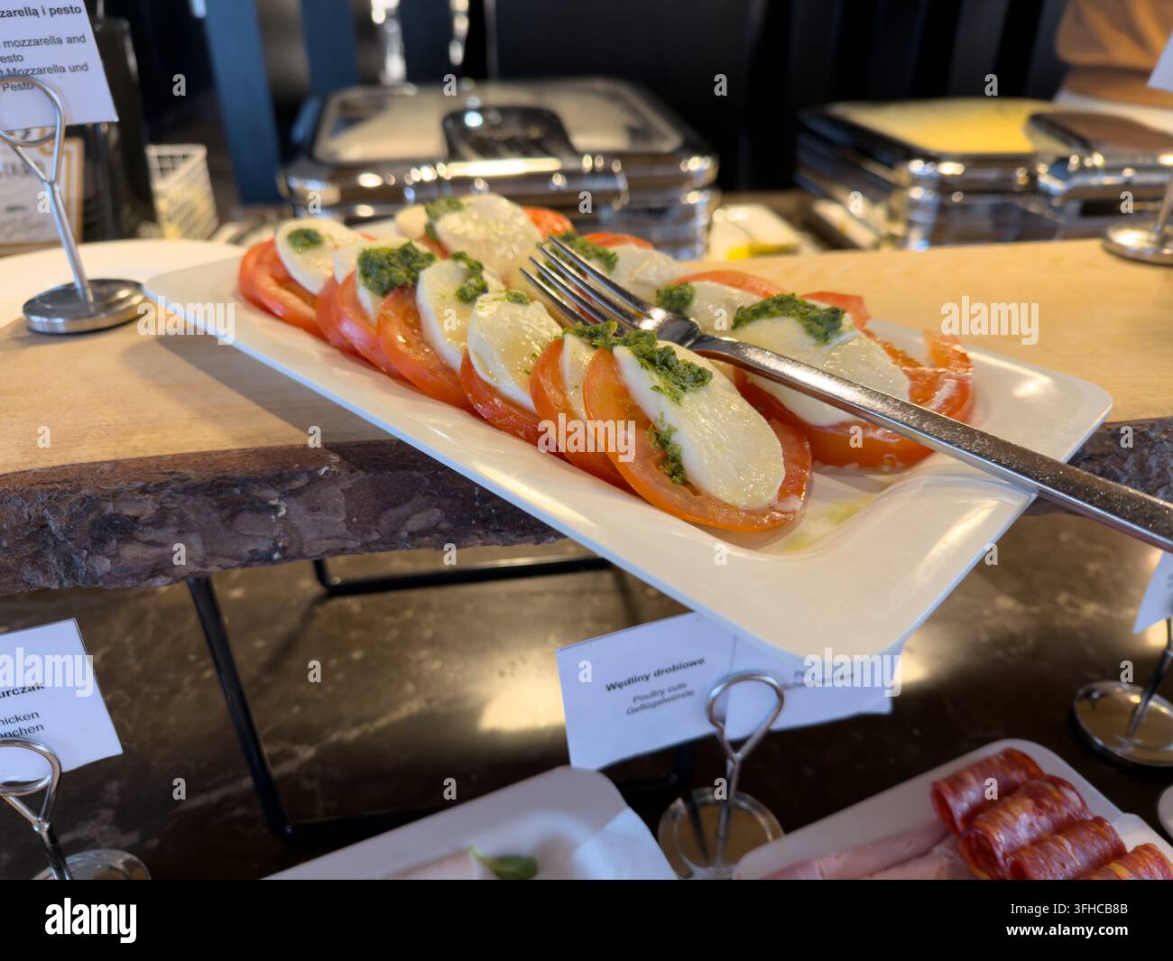 Piatto elegante di classica insalata caprese con pomodori rossi maturi, mozzarella cremosa e pesto verde vivace, pronto per il self-service in un buffet d'albergo Foto Stock
