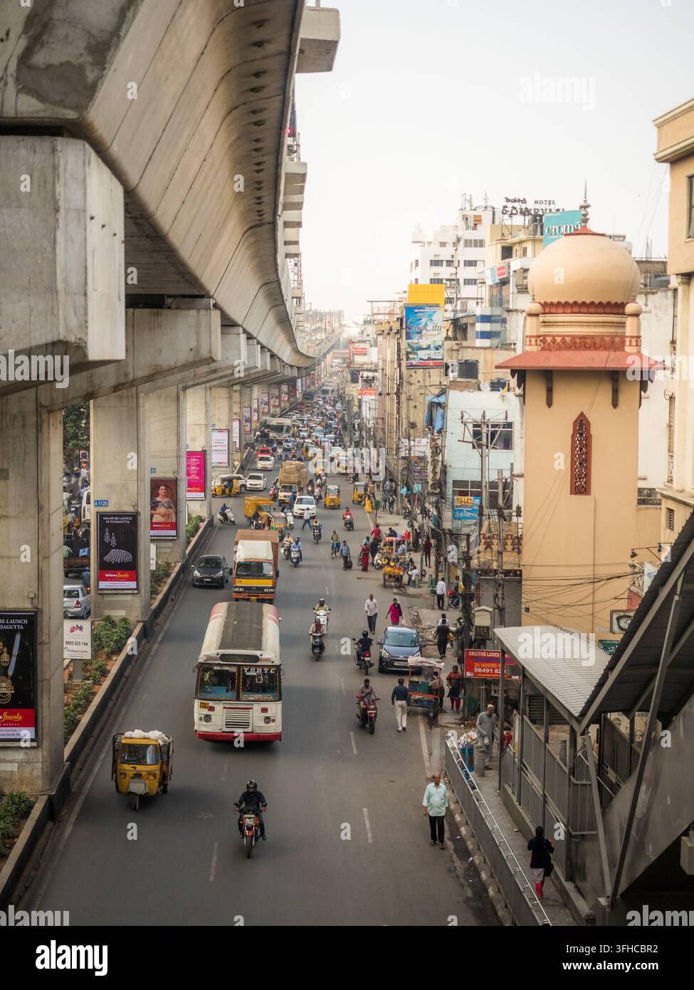 Traffico sulla Panjagutta Road sotto un viadotto della metropolitana sopraelevato a Hyderabad, Telangana, India, con autobus, auto-rickshaw, motociclette e pedoni Foto Stock