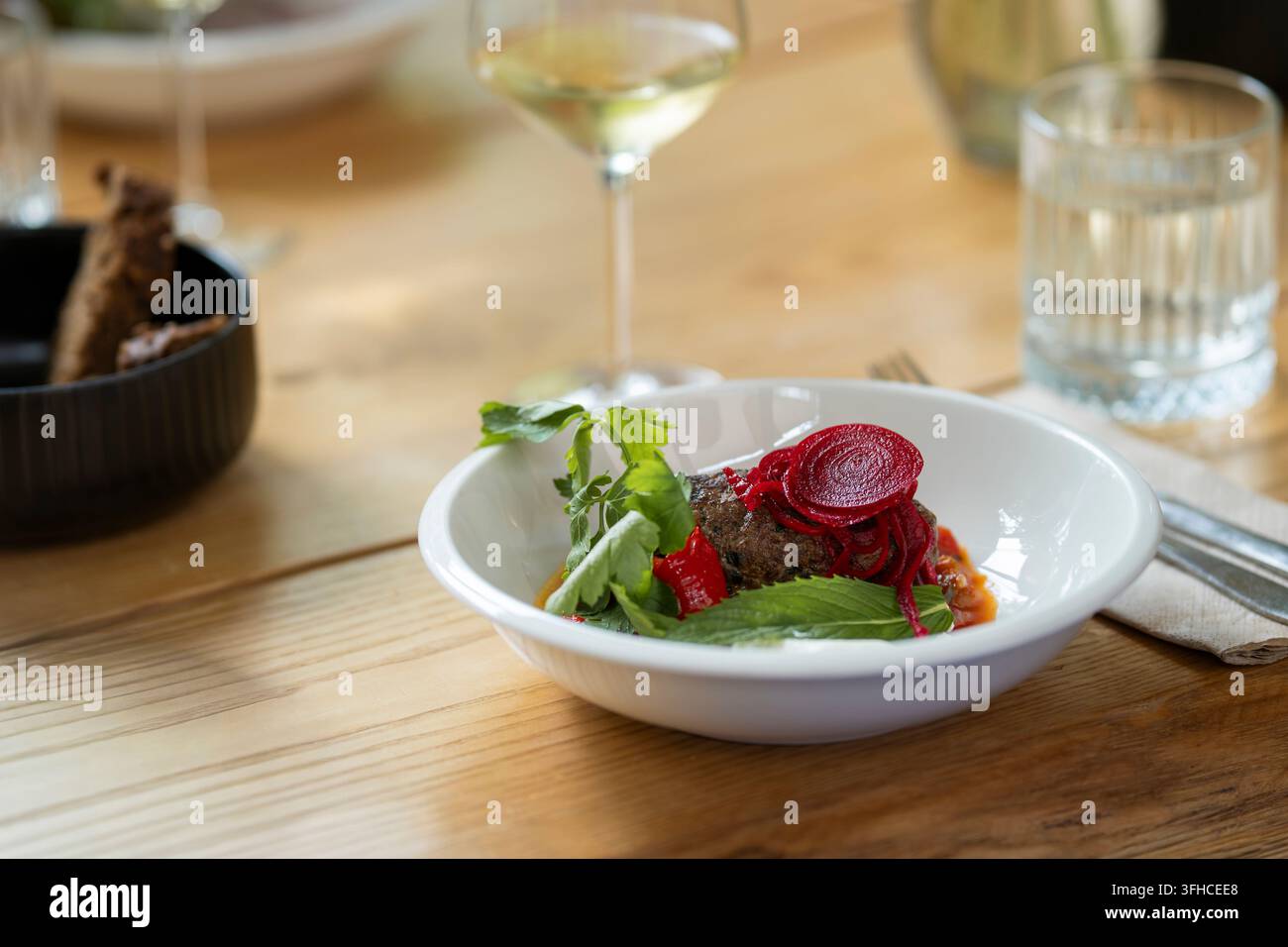 Polpetta di manzo servita con barbabietola sottaceto vivace, prezzemolo fresco e menta, pepe rosso e salsa saporita in una ciotola bianca. Il piatto di carne meravigliosamente presentato Foto Stock