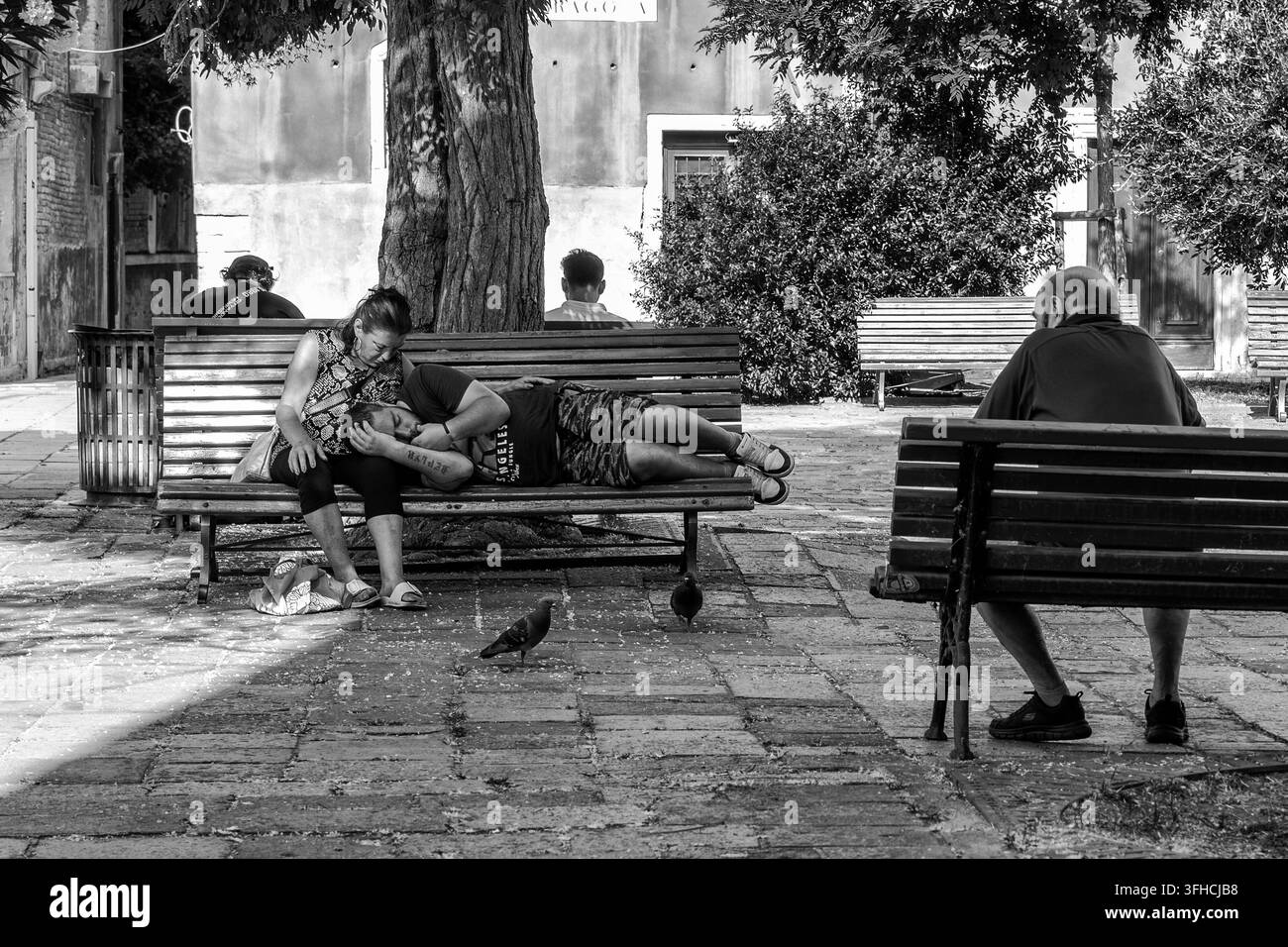 Foto in bianco e nero di un uomo che dorme con la testa sul grembo di una donna su una panchina a Campo Bandiera e Moro Bragora a Venezia, Italia Foto Stock