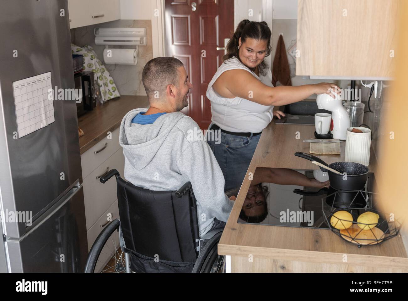 Due persone sono in una cucina a preparare un pasto. Un'assistente personale aiuta una persona disabile in sedia a rotelle. Foto Stock