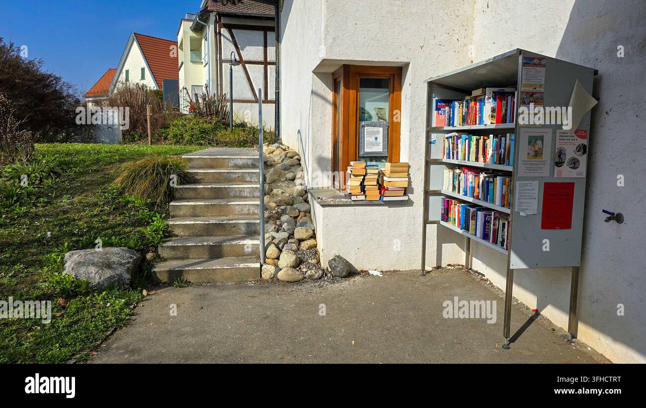 Nussdorf, Uberlingen, Germania – 16 maggio 2026. Punto di Bookcrossing con scaffale aperto e pile di libri vicino alle scale in pietra. Foto Stock