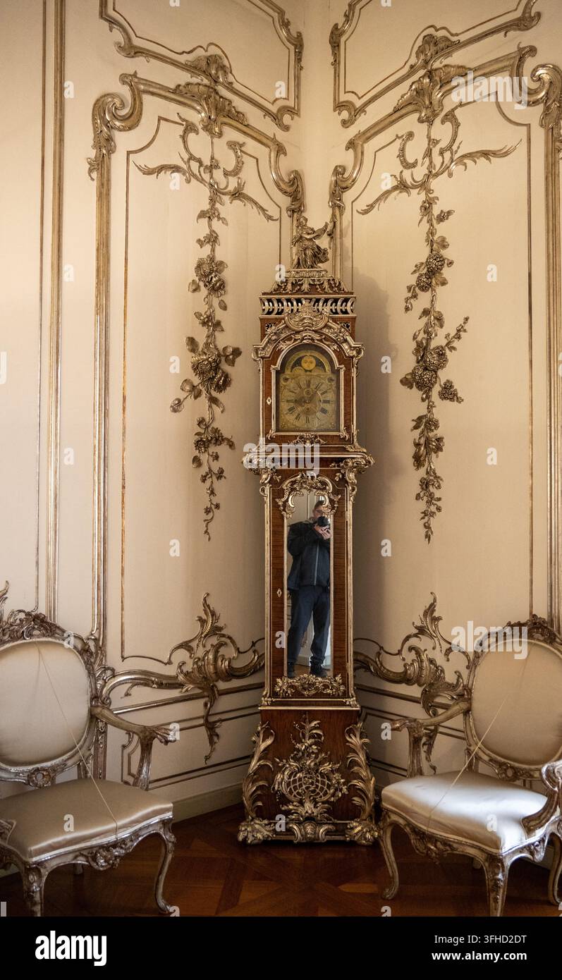 Berlino, Germania - 8 nov 25: Un orologio a pendolo decorato si trova tra pannelli murali dorati all'interno del Palazzo di Charlottenburg a Berlino. Foto Stock