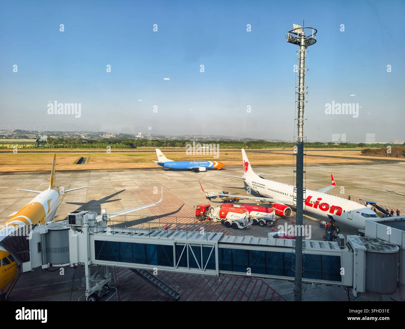 Vista del tarmac con un aereo della Lion Air parcheggiato collegato a una passerella, insieme a attrezzature di servizio a terra, camion cisterna, aeroporto di Semarang Foto Stock