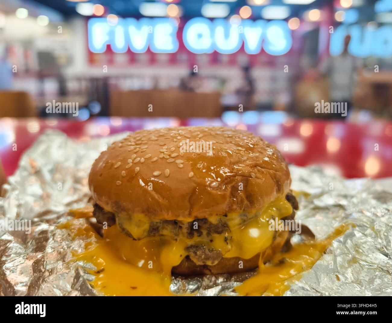 Succoso cheeseburger Five Guys servito su carta stagnola increspata con formaggio fuso che cola dal panino ai semi di sesamo. Singapore Foto Stock