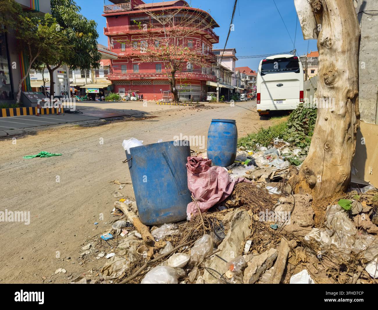 Rifiuti abbandonati, tra cui sacchetti di plastica, detriti e barili di plastica ammucchiati lungo un bordo stradale polveroso accanto a un tronco d'albero, Kampong Cham, Cambogia Foto Stock