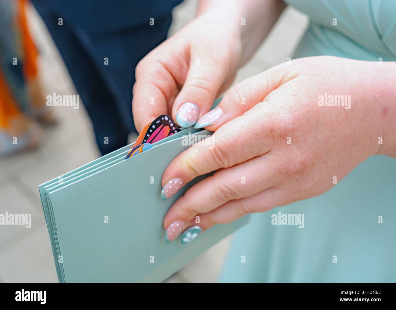 Primo piano di mani con nail art che tengono una cartella in un ambiente interno, possibilmente ufficio o casa, con carta e materiali plastici, neutro a Foto Stock
