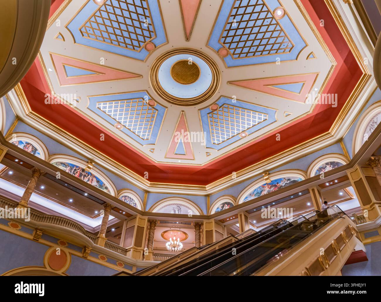 Un soffitto ottagonale elaborato con disegni geometrici dorati, blu e rossi sovrasta un atrio su più livelli con scale mobili e balconi. Foto Stock