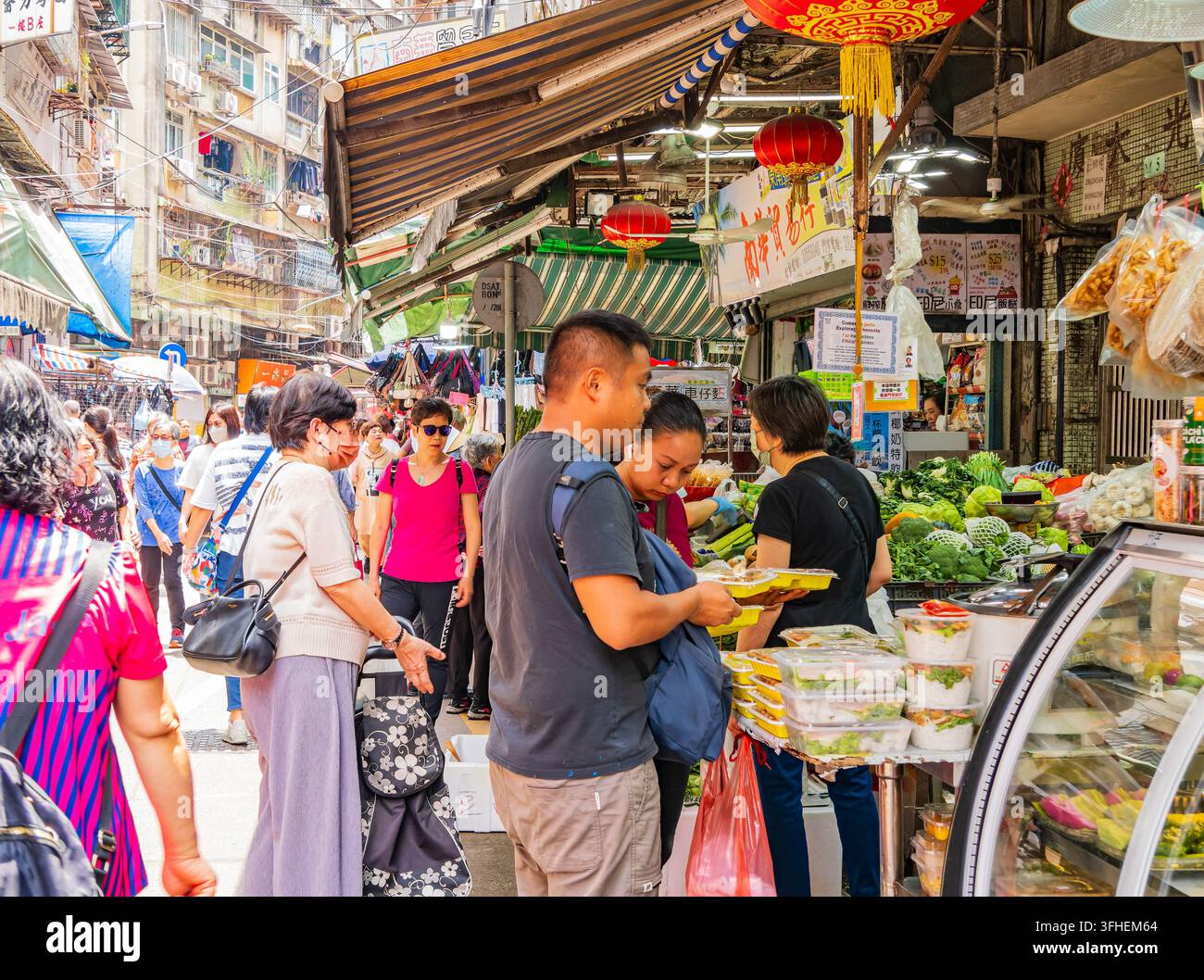 Macao, Cina, 15 apr 2024 – I clienti esaminano ortaggi preconfezionati e verdure fresche mentre i venditori sistemano le bancarelle sotto lanterne rosse. Foto Stock