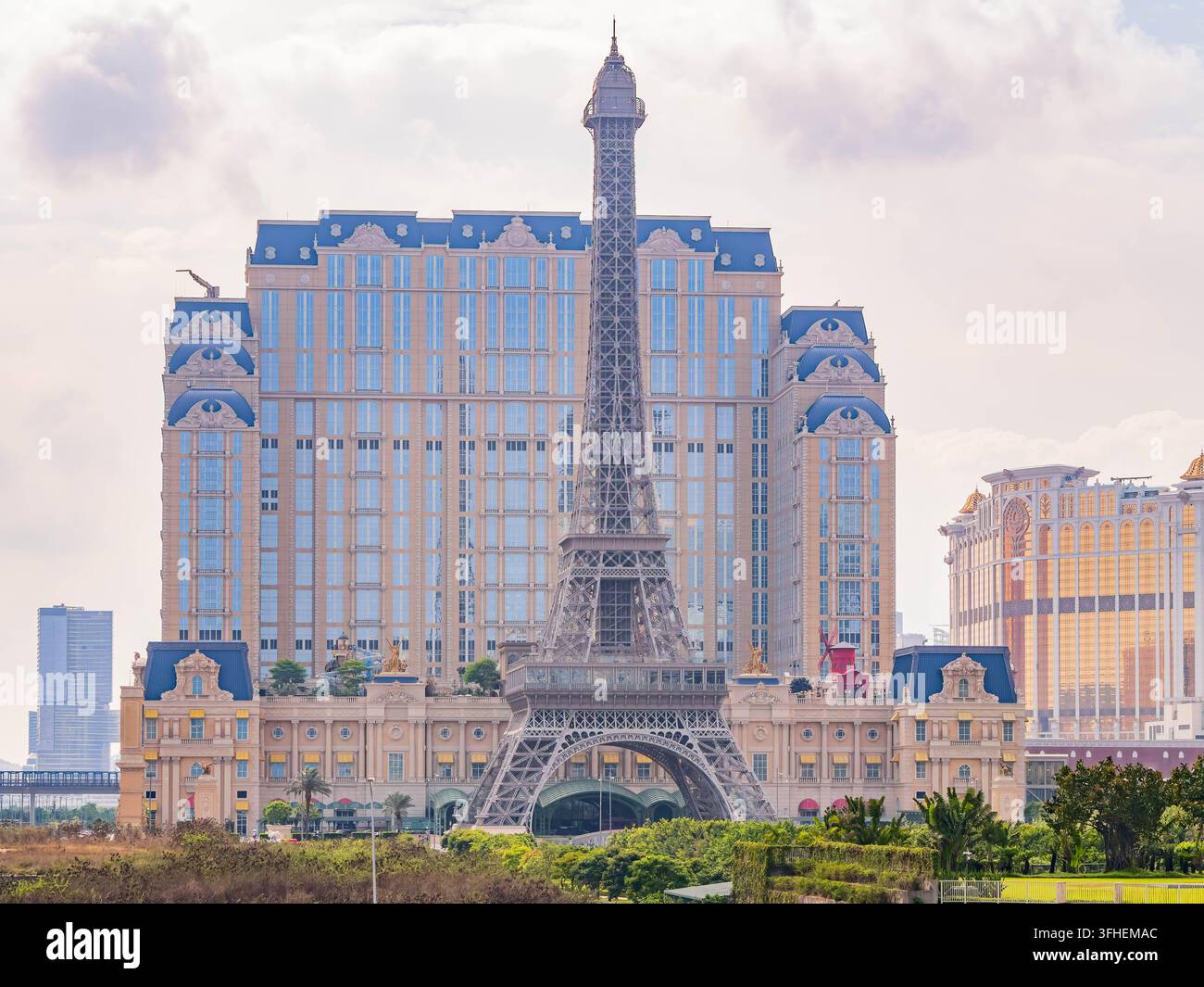 Macao, Cina, 16 apr 2024 – Una struttura metallica imponente che ricorda la Torre Eiffel si erge davanti a un maestoso hotel beige con tetti mansardati blu Foto Stock