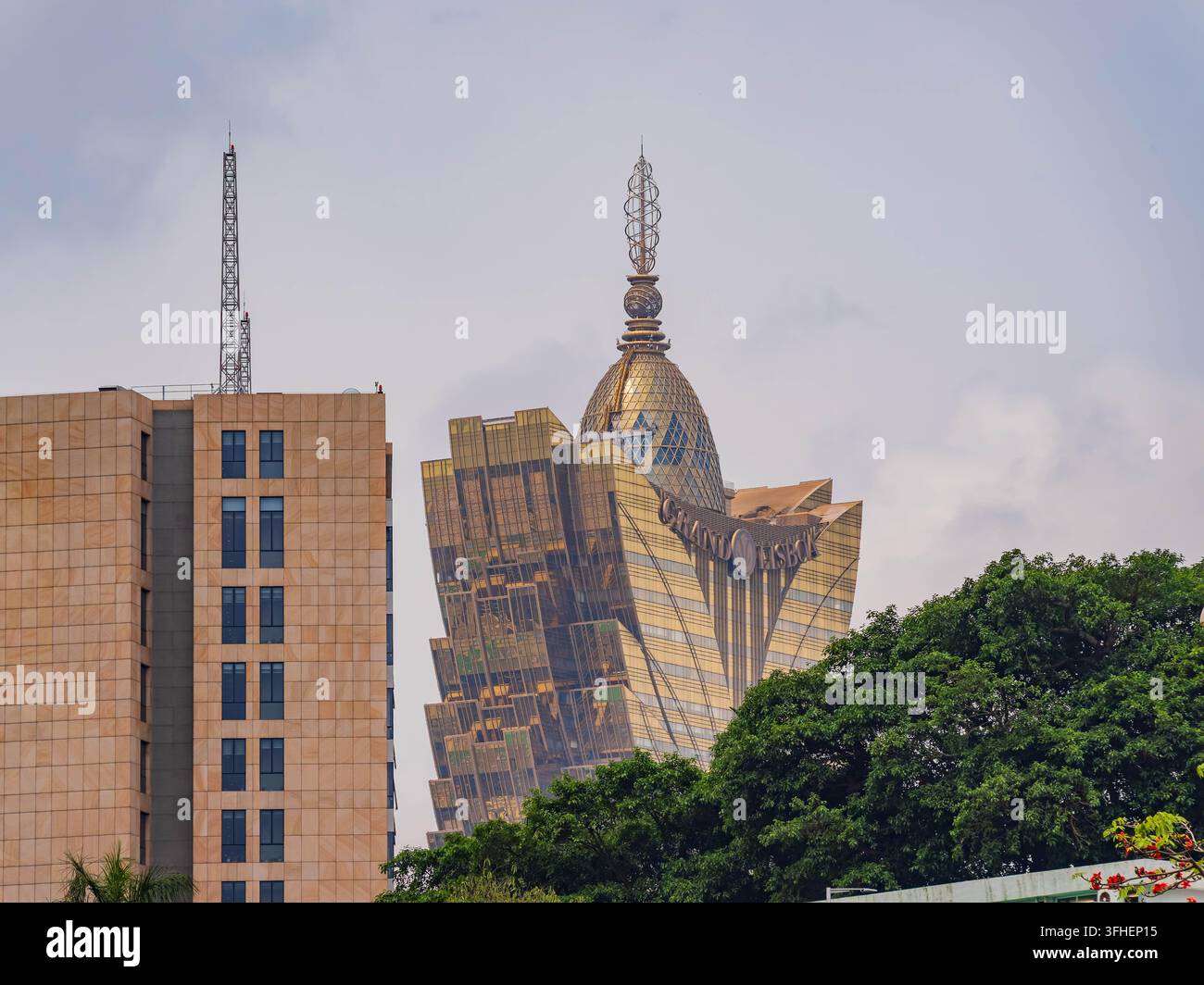 Macao, Cina, 16 apr. 2024 – Grattacieli dorati con pinnacoli distintivi si ergono maestosamente sopra una vegetazione lussureggiante in un contesto urbano vivace. Foto Stock