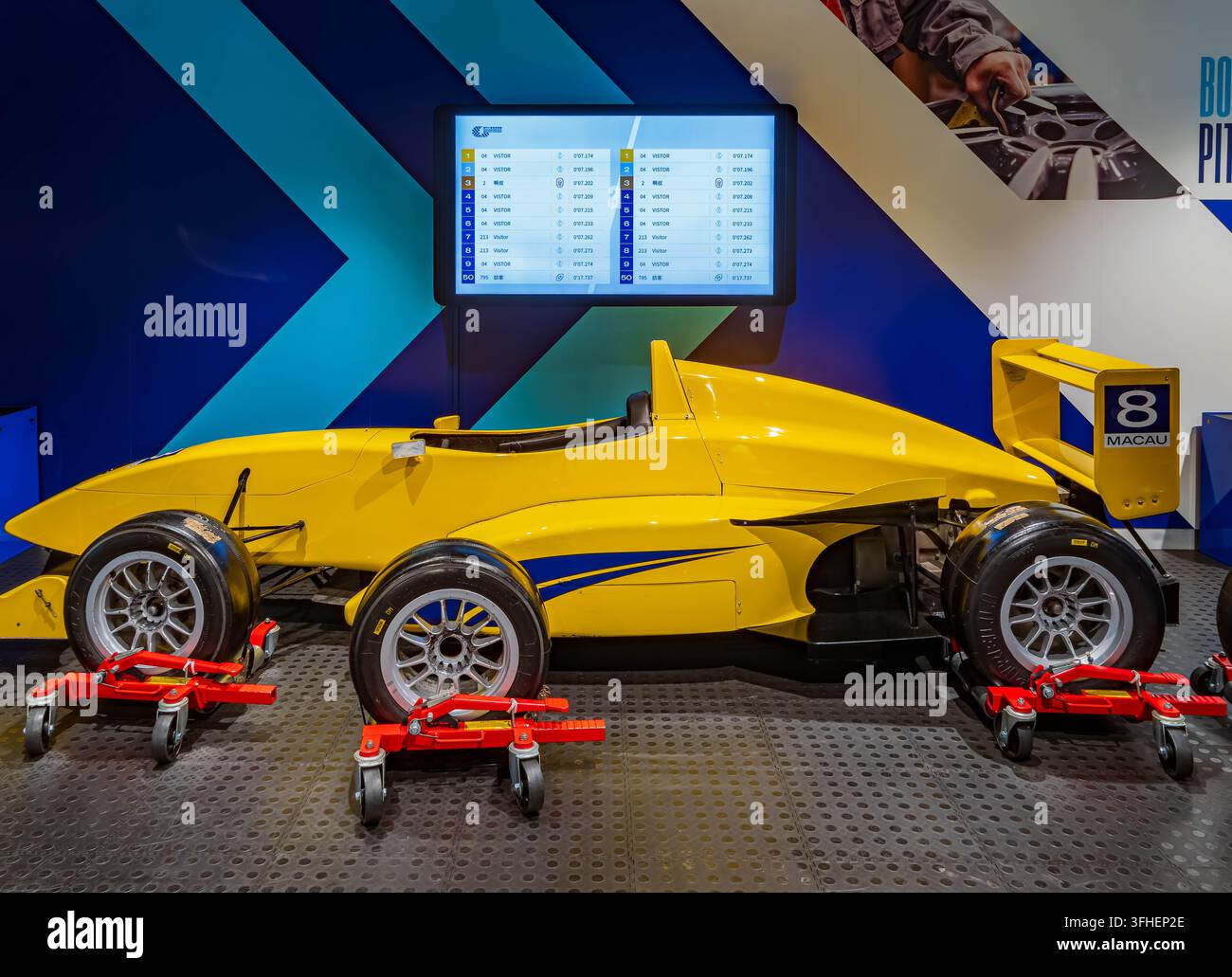 Un'auto da corsa a ruote aperte gialla con il numero 8 e il testo Macau sull'ala posteriore poggia su puntoni rossi davanti a uno schermo di cronometraggio digitale. Foto Stock