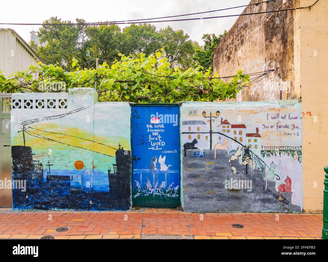 Macao, Cina, 17 APR 2024 – Un murale vivace illustra un paesaggio urbano al tramonto e una scena di strada con gatti giocosi accanto a motivi biblici cristiani Foto Stock