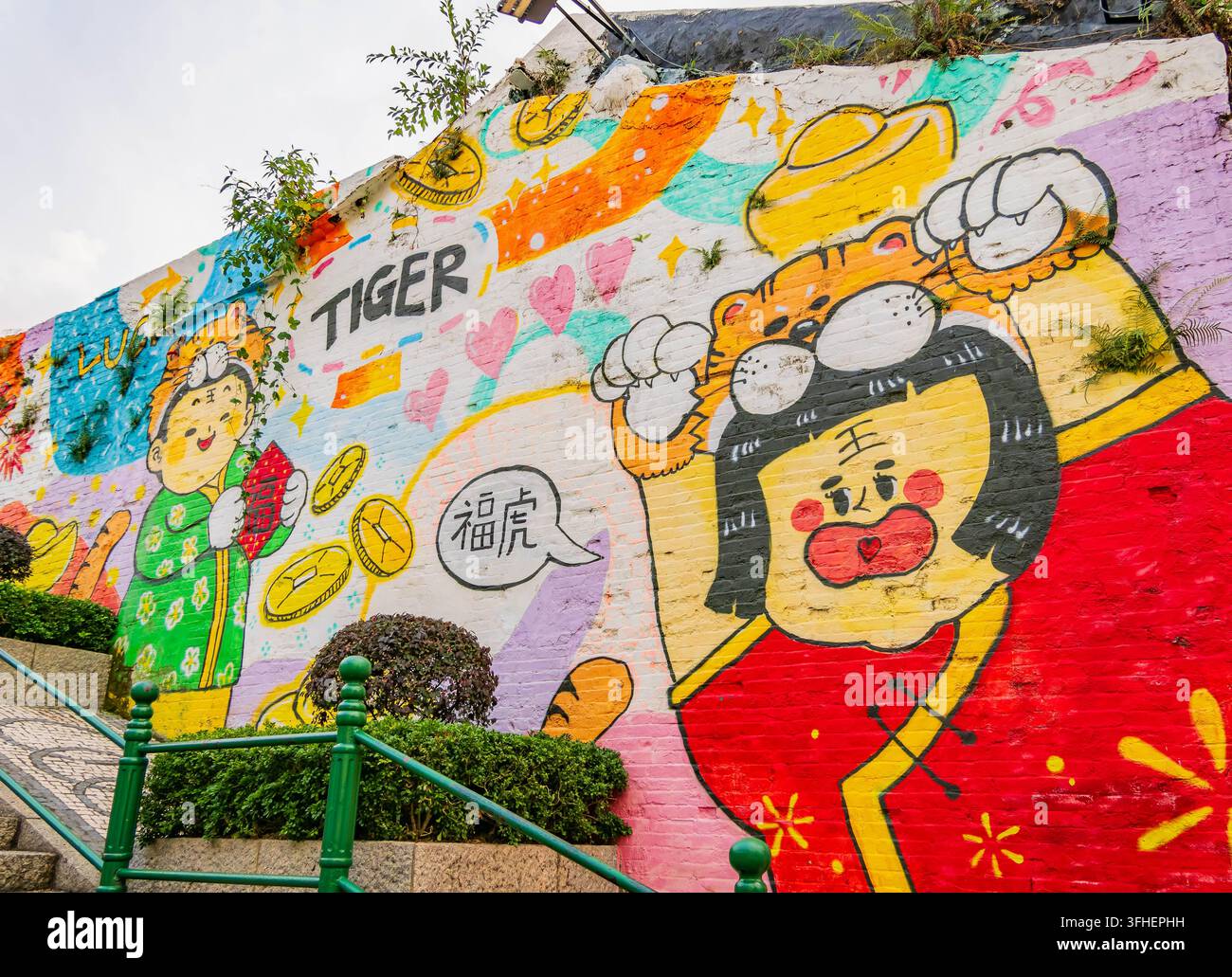 Macao, Cina, 17 apr 2024 – Un'arte di strada vivace raffigura tigri dei cartoni animati in abiti rossi festivi, circondati da monete d'oro, cuori rosa e Foto Stock