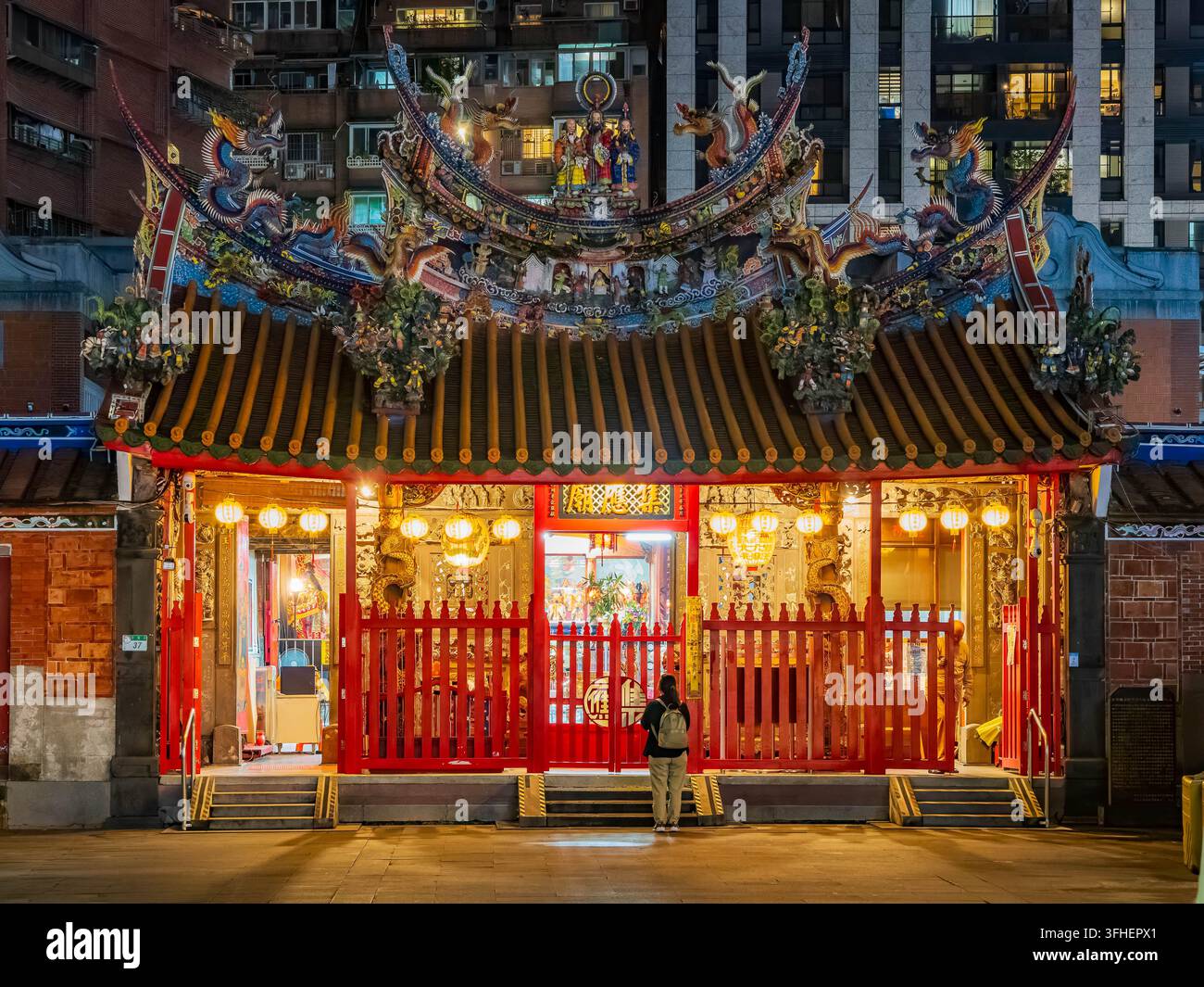Taipei, Taiwan, 19 apr. 2024 – Una persona osserva l’ingresso luminoso di un tempio tradizionale ornato con elaborate decorazioni di draghi sul tetto e Foto Stock