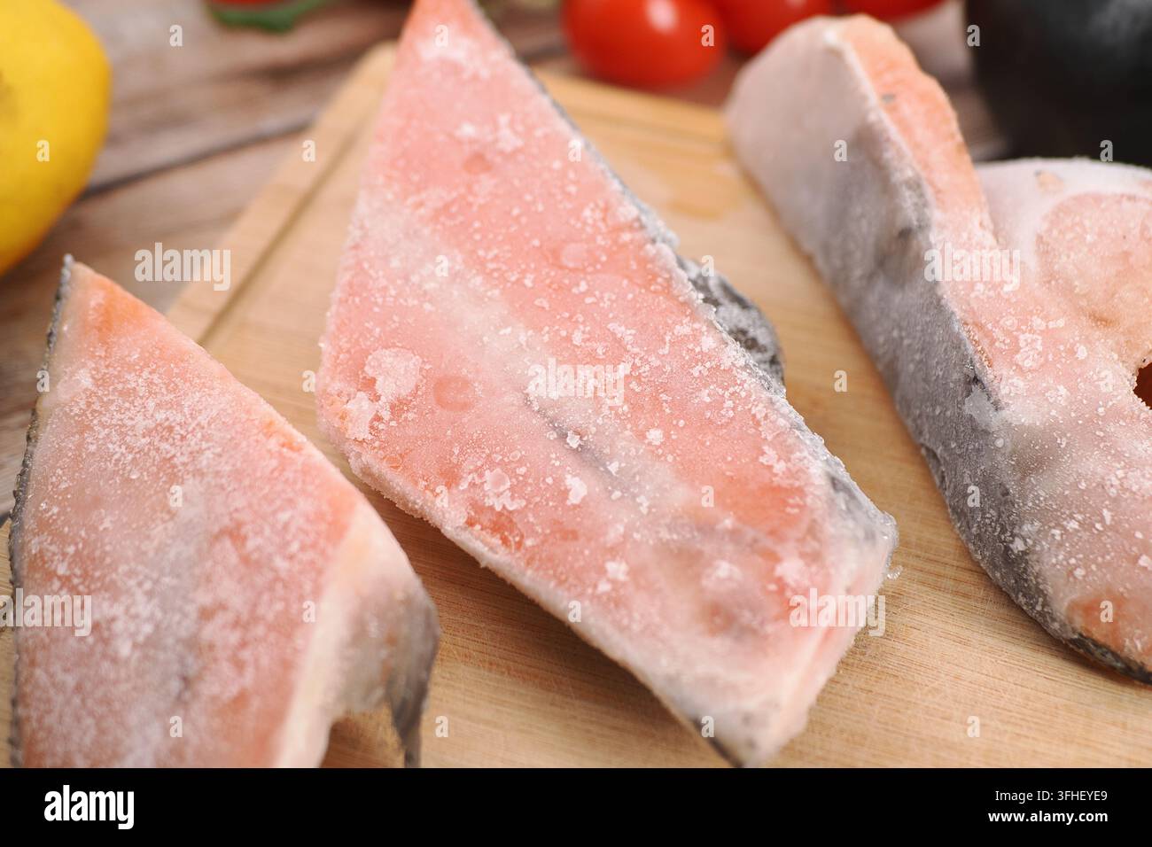 Filetti di pesce congelati su un tagliere di legno con verdure e limone Foto Stock