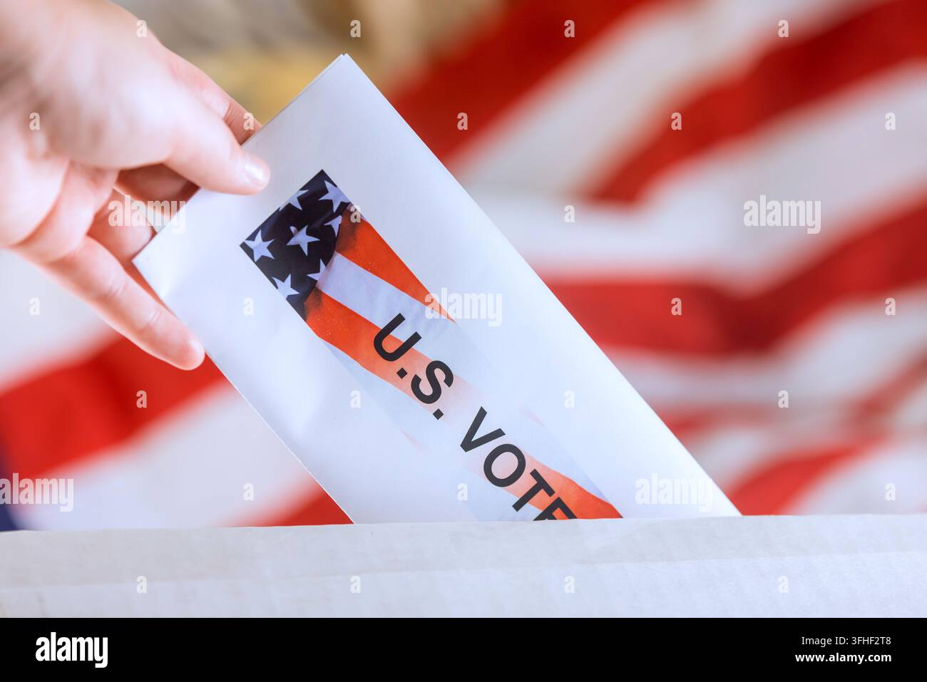 Una mano mette una scheda elettorale in un'urna, con una bandiera americana sullo sfondo durante un'elezione. Foto Stock