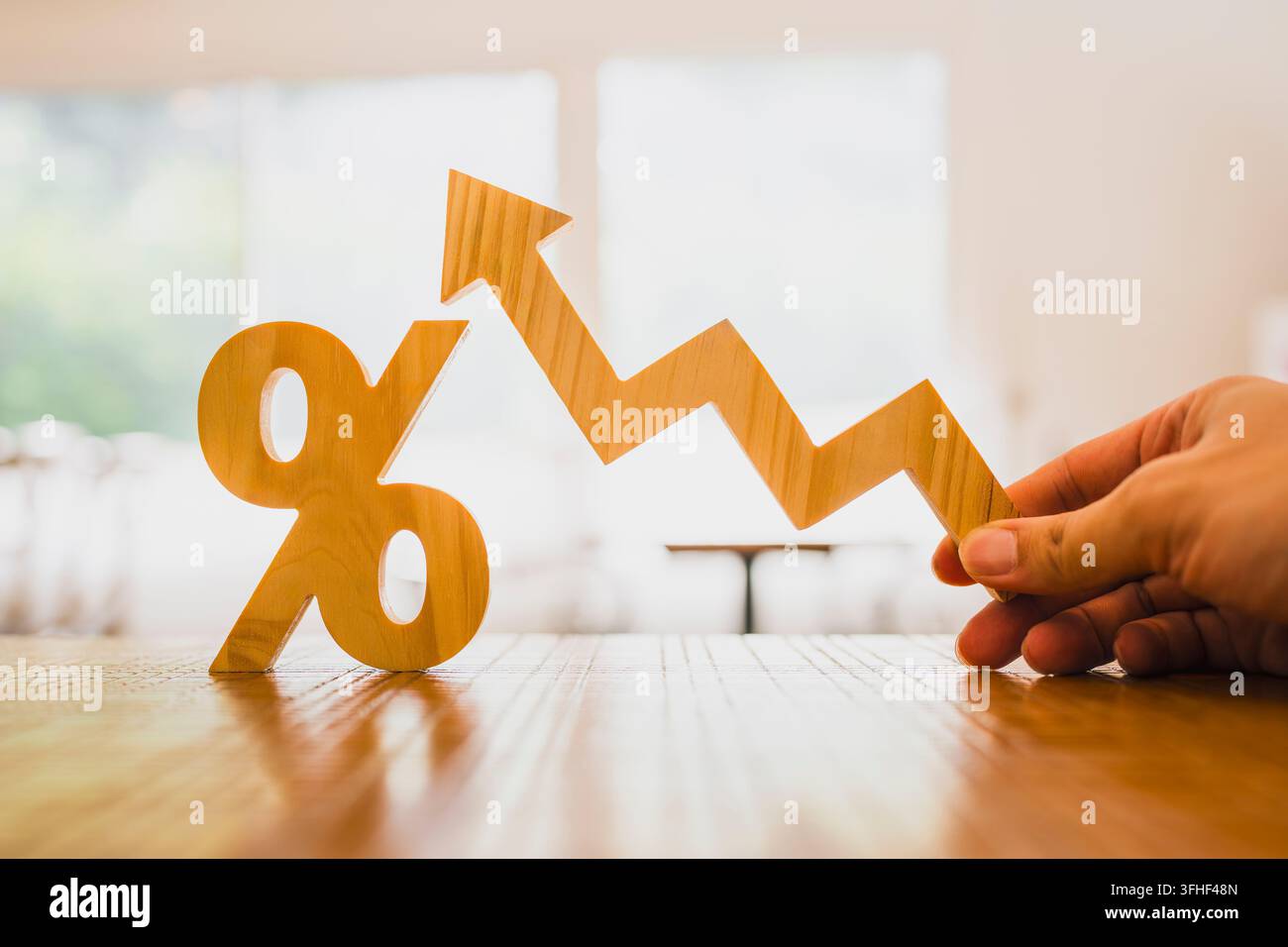Concetto di aumento dei tassi di interesse e crescita economica, mano che tiene una freccia a zigzag verso l'alto accanto a un segno percentuale in legno sul tavolo, rappresentante l'inflazione Foto Stock