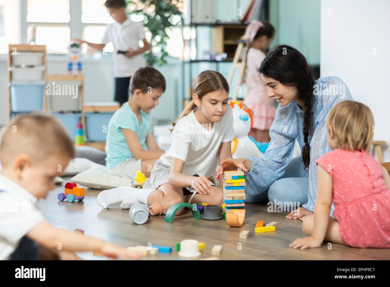 Bambini diversi e amichevoli che si divertono con giochi educativi vicino a un mentore in un centro creativo Foto Stock