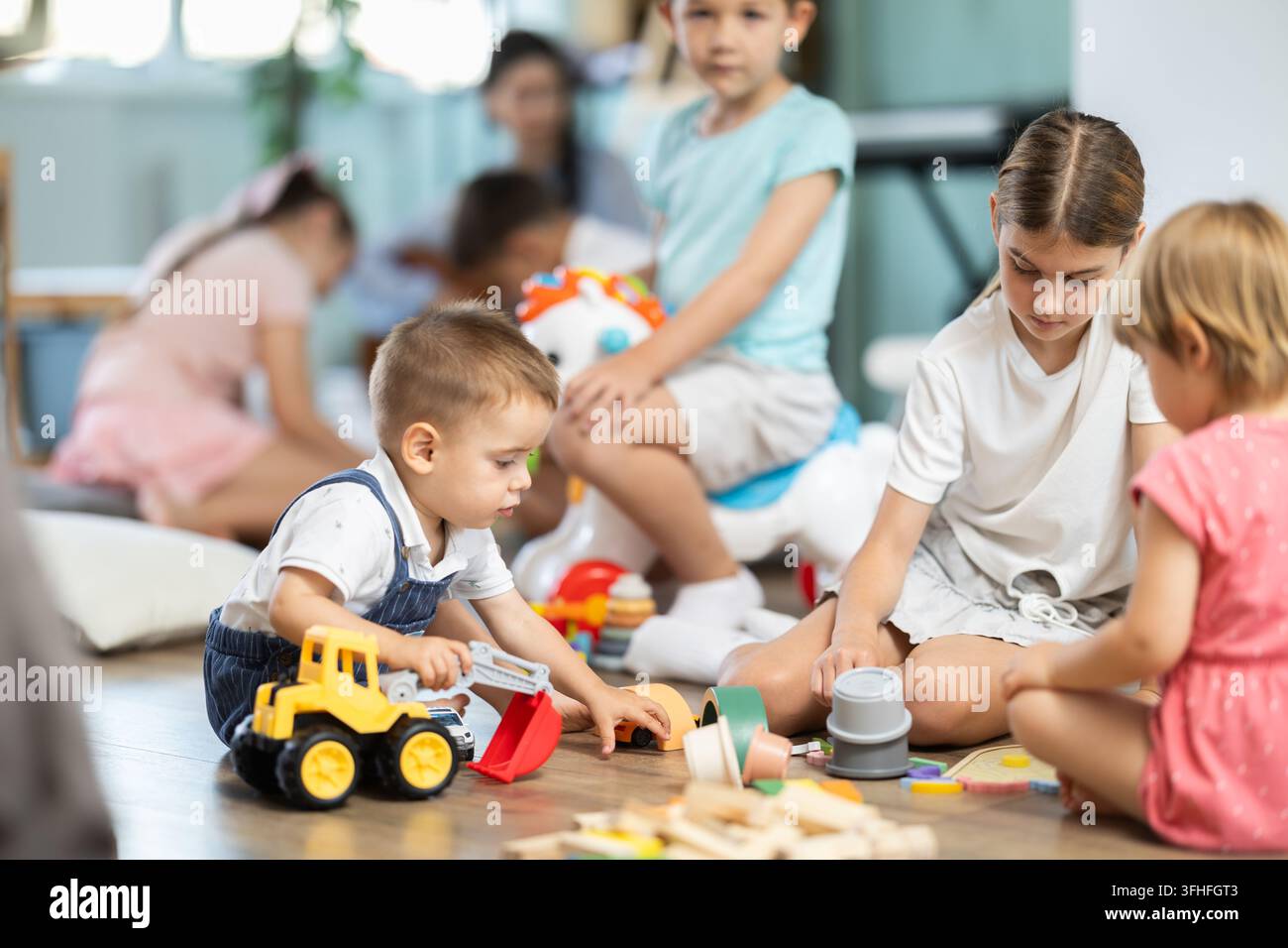 Bambini che giocano con giocattoli seduti sul pavimento nell'asilo Foto Stock
