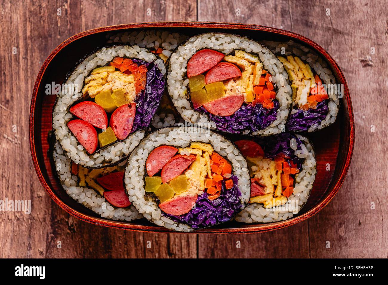 Kimbap (o gimbap) colorato con verdure e salsiccia in una scatola di legno su una superficie di legno Foto Stock