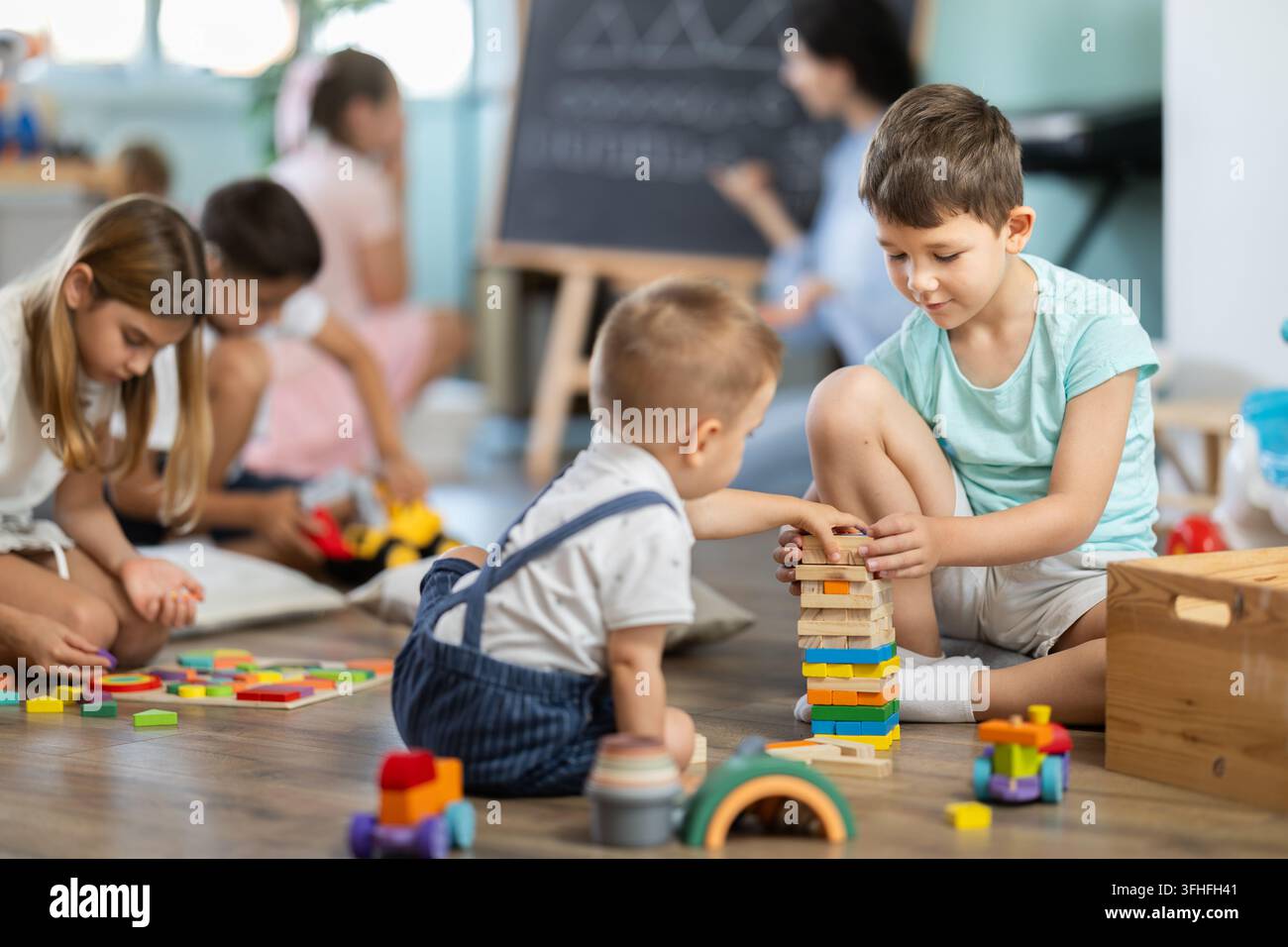 Bambini che giocano con giocattoli seduti sul pavimento nell'asilo Foto Stock
