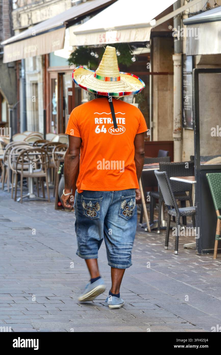 Uomo nero con maglietta arancione e sombrero alto che cammina lungo una strada stretta nel quartiere vecchio di Tours, Indre-et-Loire (37), Francia. Foto Stock