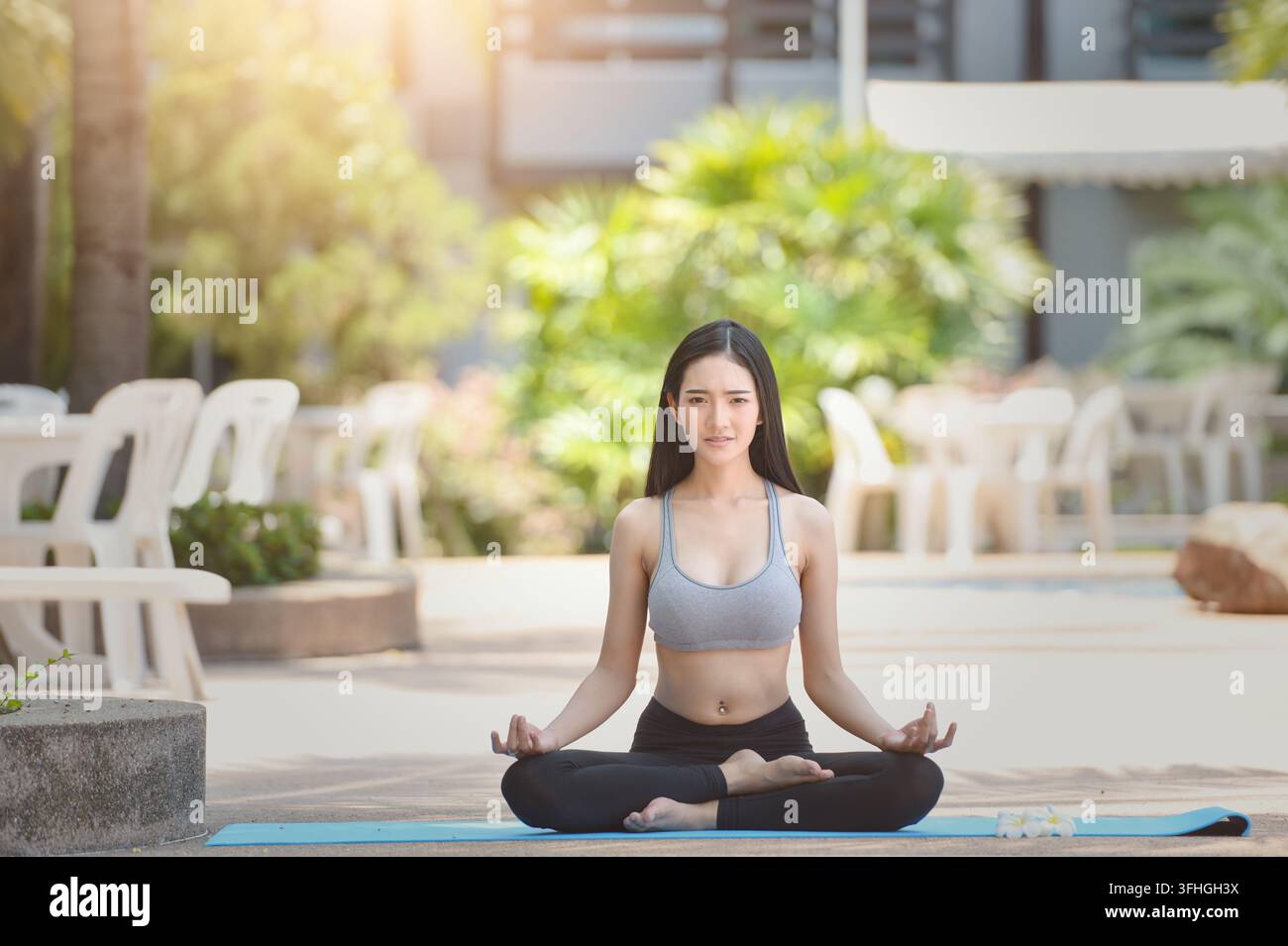Giovane donna in abbigliamento sportivo seduta all'aperto in una posizione yoga a gambe incrociate nel Padmasana (lotus) con le mani in una posizione mudra del mento, che pratica la meditazione consapevole in un resort all'aperto Foto Stock