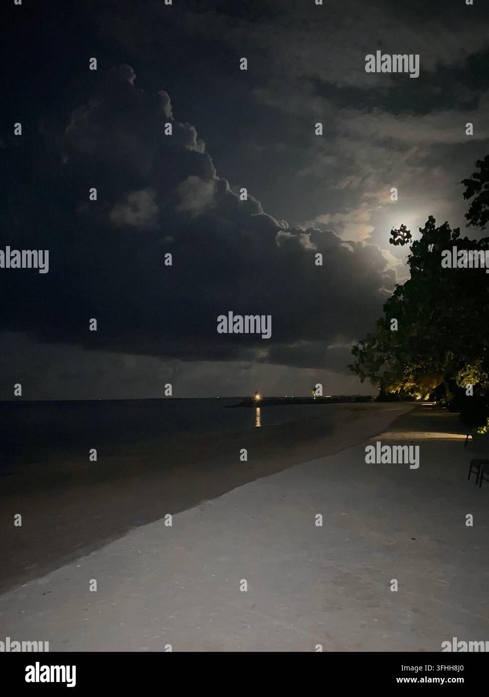 La luce della luna brilla dietro drammatiche nuvole temporalesche sopra una spiaggia tropicale deserta. - Immagine stock catturata con smartphone