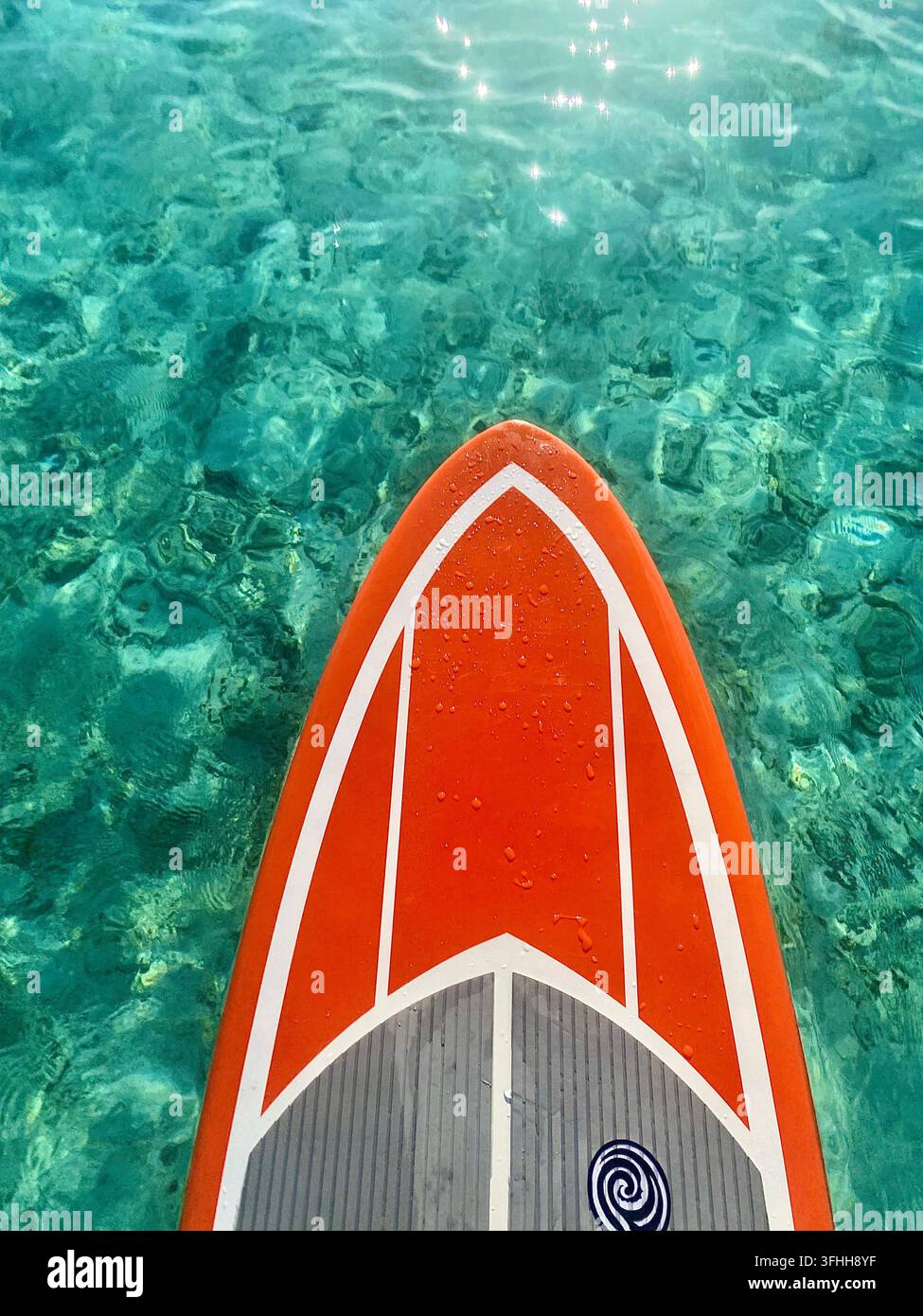 Una tavola da paddle arancione galleggia su una laguna turchese chiara sotto la luce tropicale scintillante. - Immagine stock catturata con smartphone
