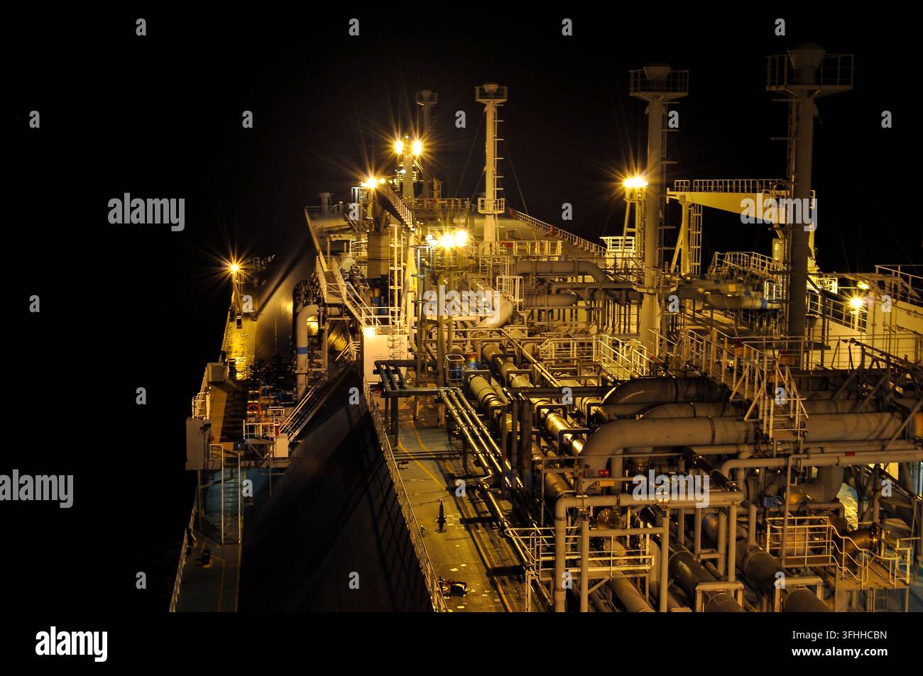 Ponte e sistemi di tubazioni di una nave portatrice di LNG illuminati durante le operazioni notturne in mare Foto Stock