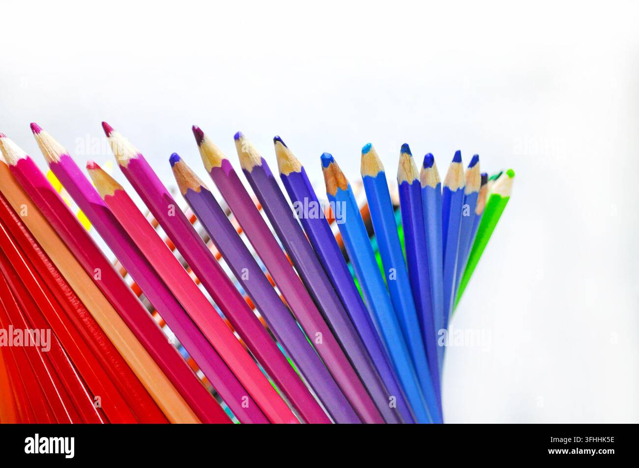 Matite colorate appuntite disposte a ventaglio su uno sfondo bianco con ampio spazio per il testo, rappresentando creatività, disegno, educazione e arte. Foto Stock