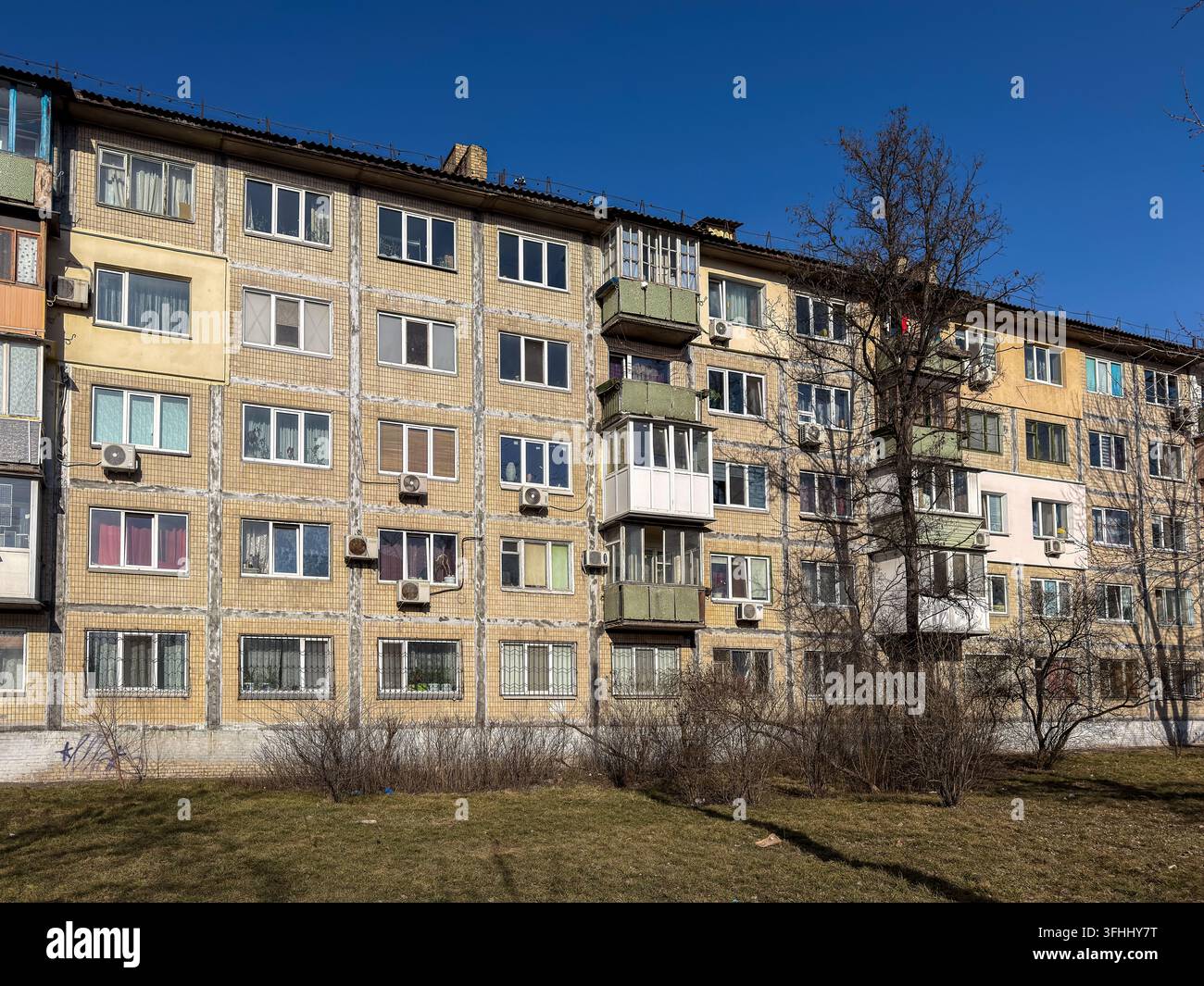 Blocco residenziale a più piani in stile sovietico con una facciata in mattoni invecchiati e vari balconi sullo sfondo di un cielo blu profondo, catturando l'architettura del Foto Stock
