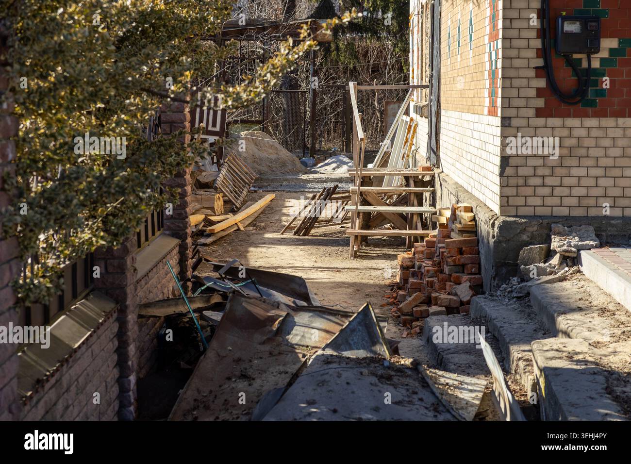 Materiali da costruzione sparsi giacciono vicino a una casa residenziale in ristrutturazione esterna, riflettendo progetti di miglioramento della casa e situazioni laboriose Foto Stock