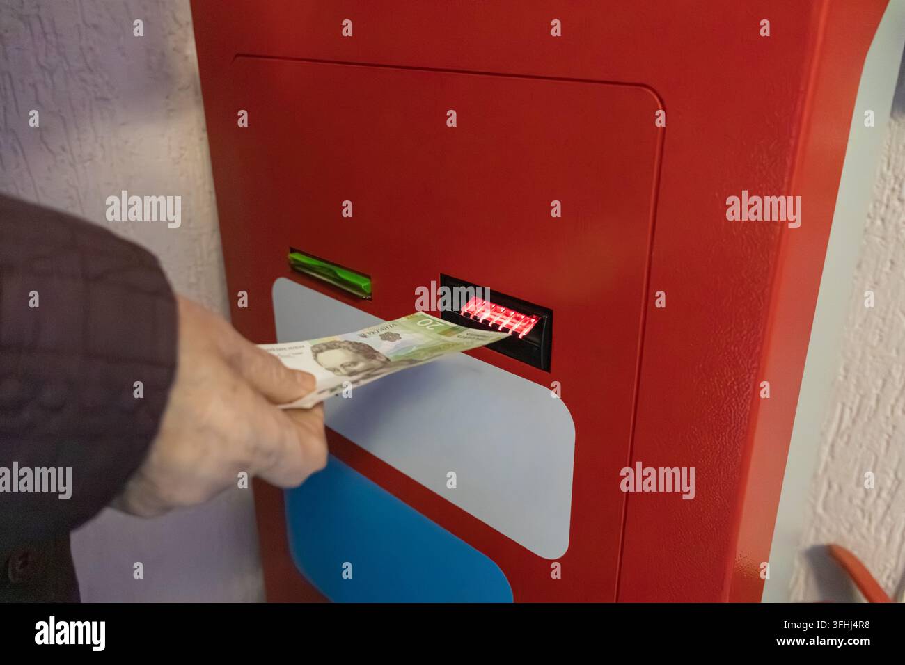 Un individuo inserisce una banconota in un chiosco di pagamento rosso vivace, illustrando un processo digitale fluido ed efficiente per completare gli acquisti al dettaglio quotidiani Foto Stock
