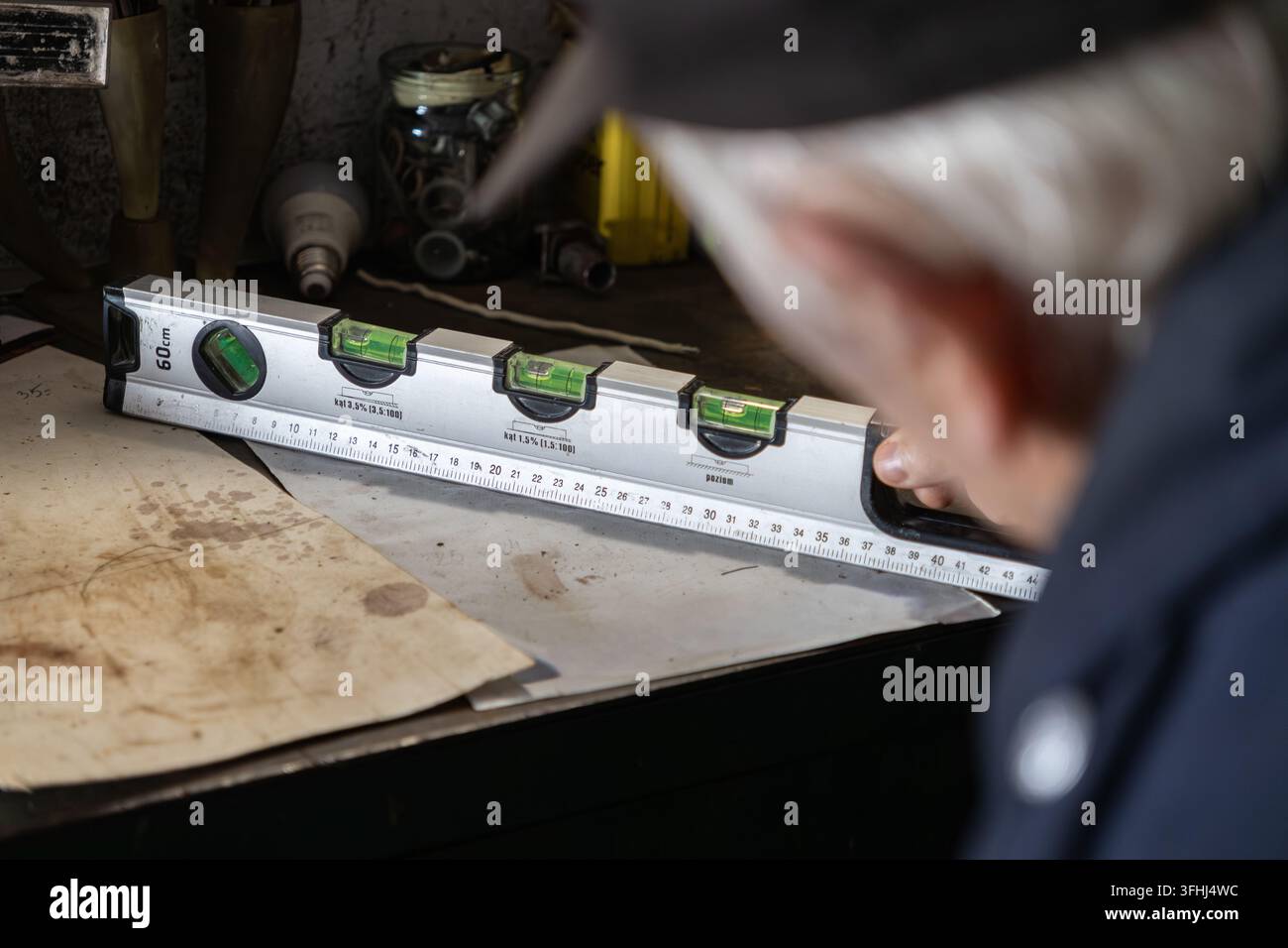 Un falegname esperto controlla l'allineamento con un livello metallico su un banco da lavoro polveroso, sottolineando dedizione, abilità di misurazione esperta, lavoro manuale Foto Stock