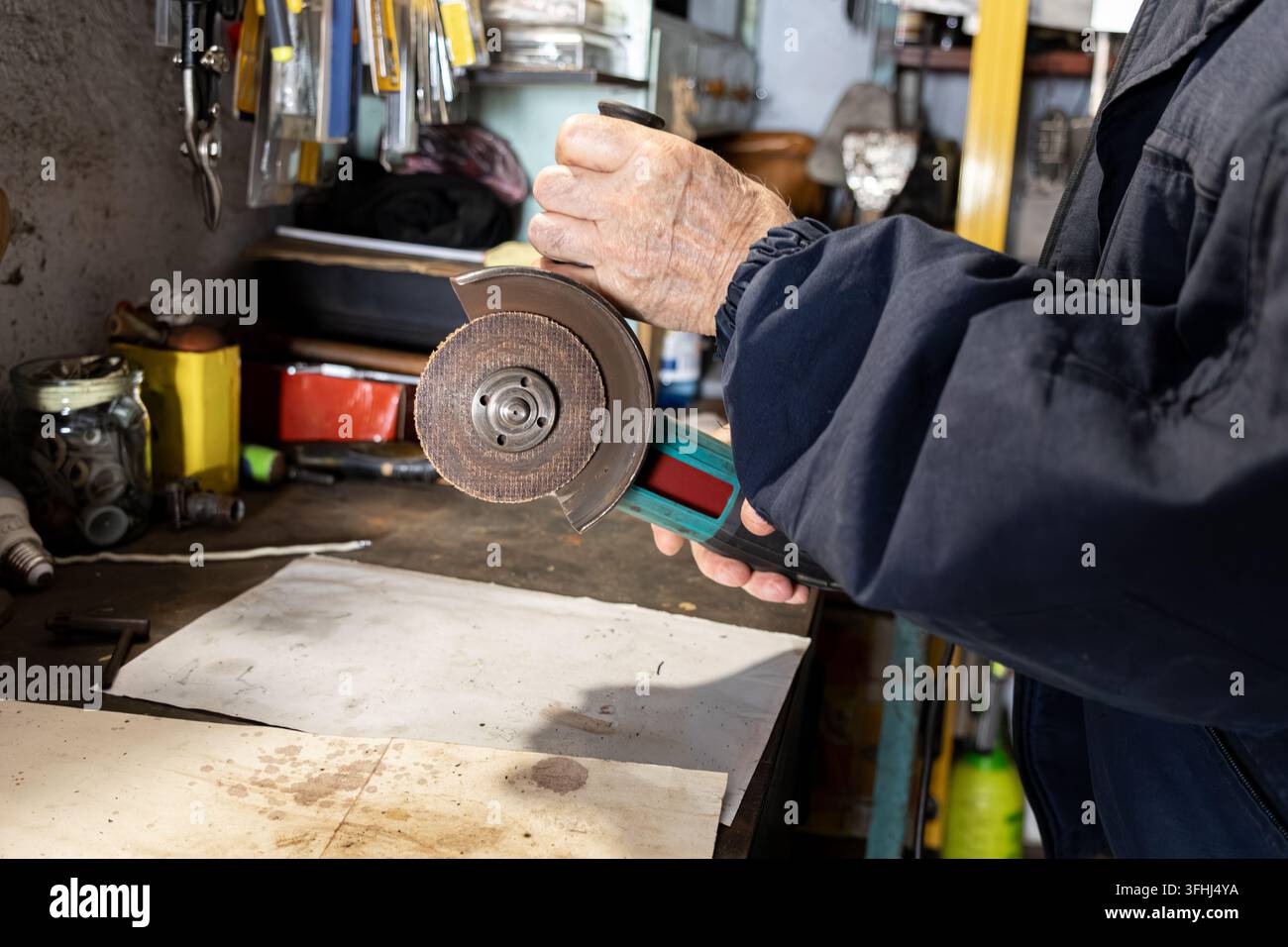Un operaio esperto aziona una smerigliatrice portatile in uno spazio di garage polveroso, illustrando competenza, artigianato industriale e duro lavoro attraverso il c Foto Stock