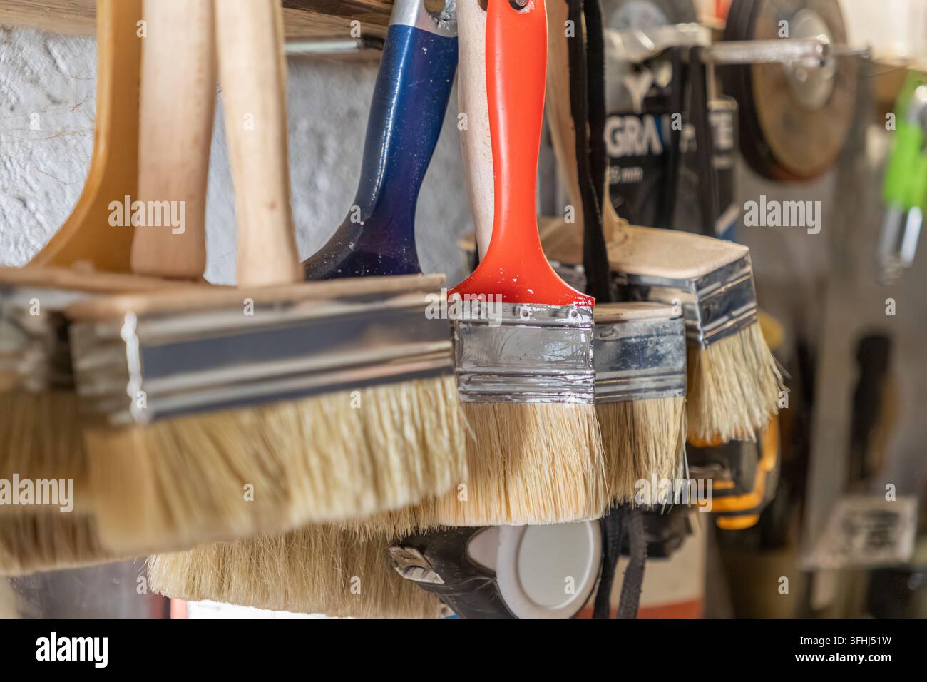 Pennelli multicolori sospesi ordinatamente contro un muro riflettono la preparazione organizzata per ristrutturazioni, lavori di casa, pittura di interni Foto Stock
