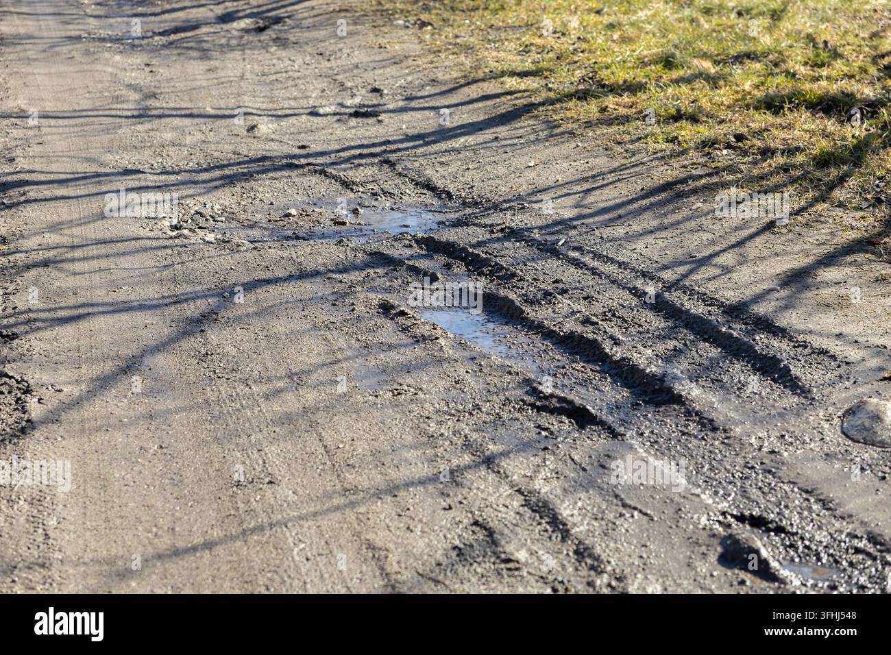 Solchi profondi scavati in un sentiero sterrato pieno di acqua piovana, evidenziando la texture ruvida di una stradina di campagna in un paesaggio segnato dai mari Foto Stock