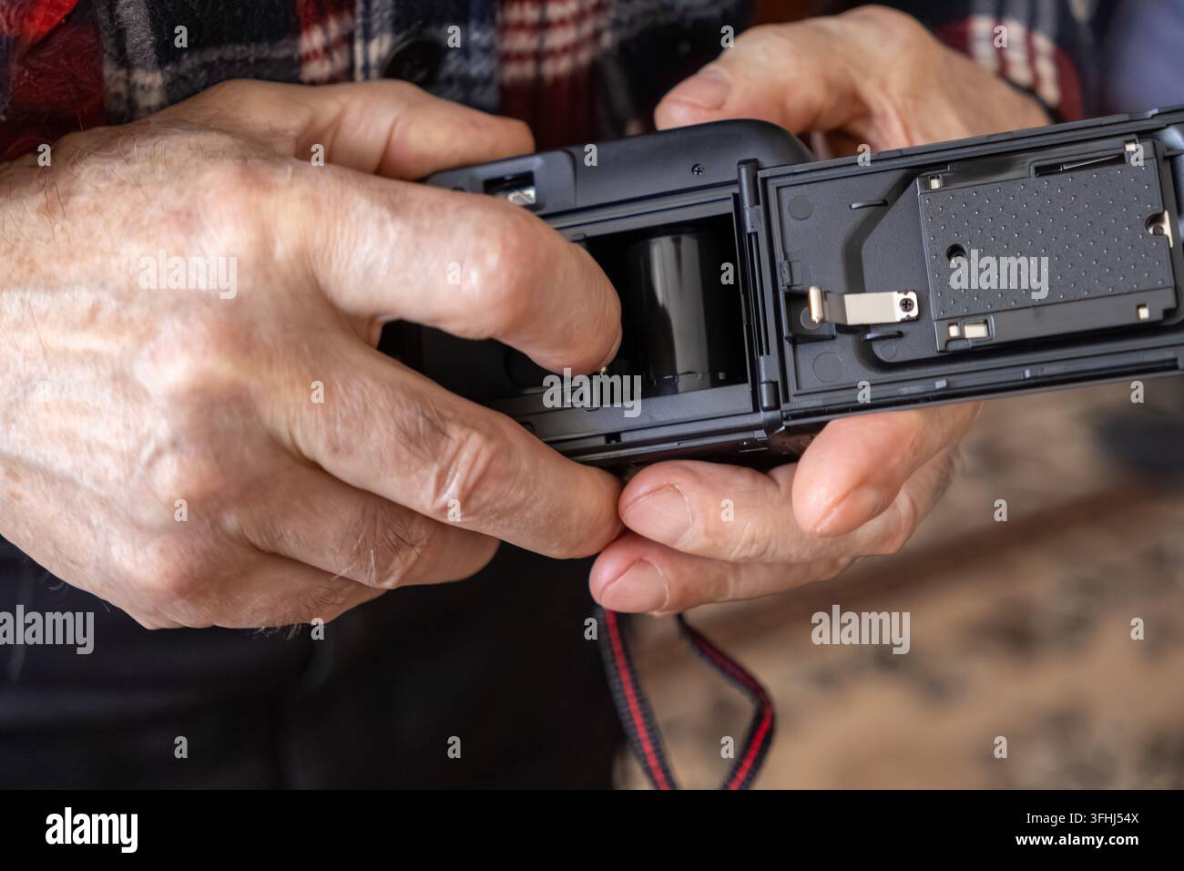 Un individuo anziano carica una pellicola 35 mm in una macchina fotografica compatta vintage, illustrando l'esperienza tattile della fotografia tradizionale in un mondo digitale Foto Stock