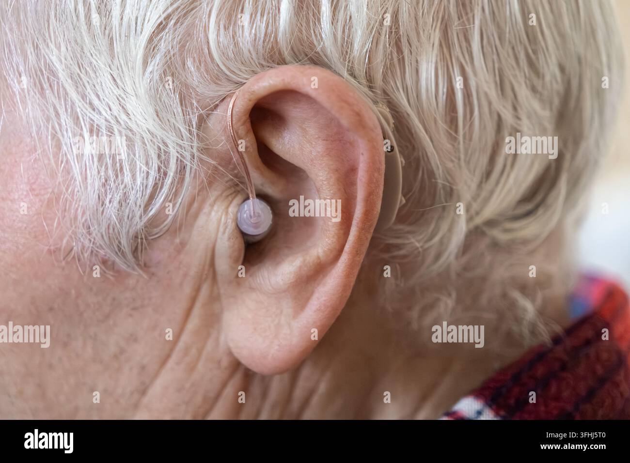 Un individuo anziano che utilizza un moderno dispositivo per l'udito per gestire le menomazioni legate all'età, riflettendo la cura e il supporto professionali di un audiologo Foto Stock