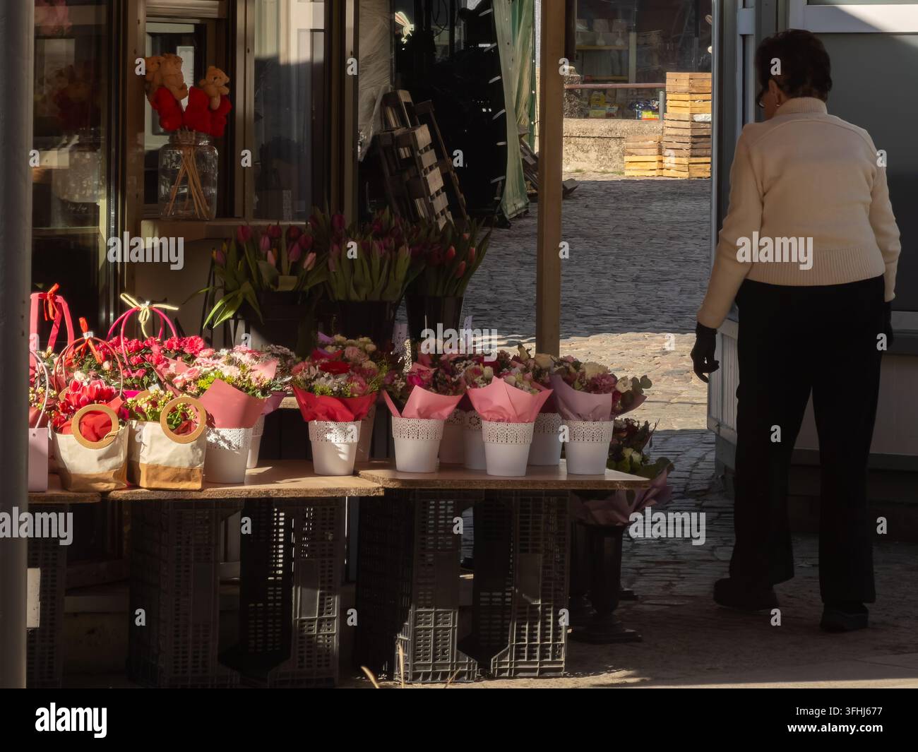 Una persona anziana passa davanti a un chiosco di fiori rifornito di fiori vivaci primaverili in una giornata soleggiata, mostrando l'attività commerciale al dettaglio in una città europea Foto Stock