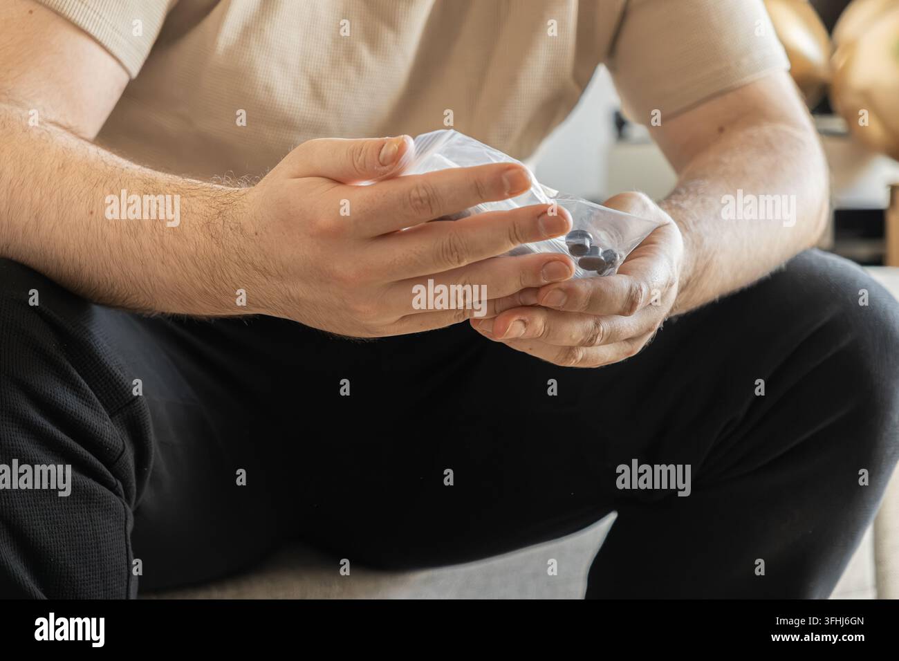 Primo piano di una persona che tiene un sacchetto di integratori scuri o compresse medicinali, catturando un momento essenziale di cura in un ambiente domestico per dare priorità Foto Stock