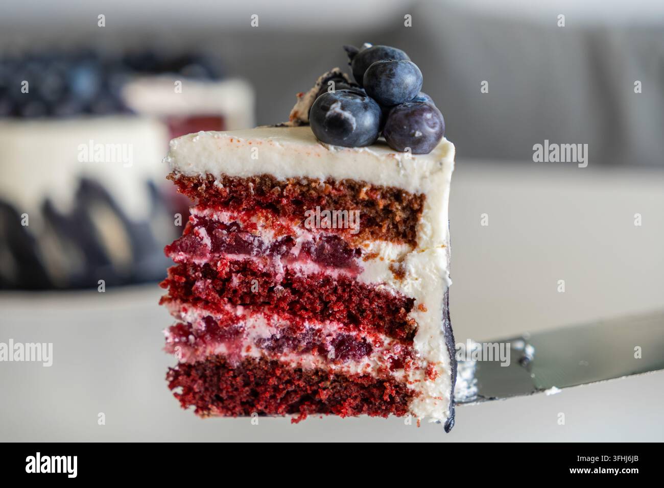 Una fetta di torta al velluto rosso a strati ricoperta di mirtilli maturi poggia su un sollevatore per torte, creando un'immagine appetitosa per la fotografia professionale del cibo e Foto Stock