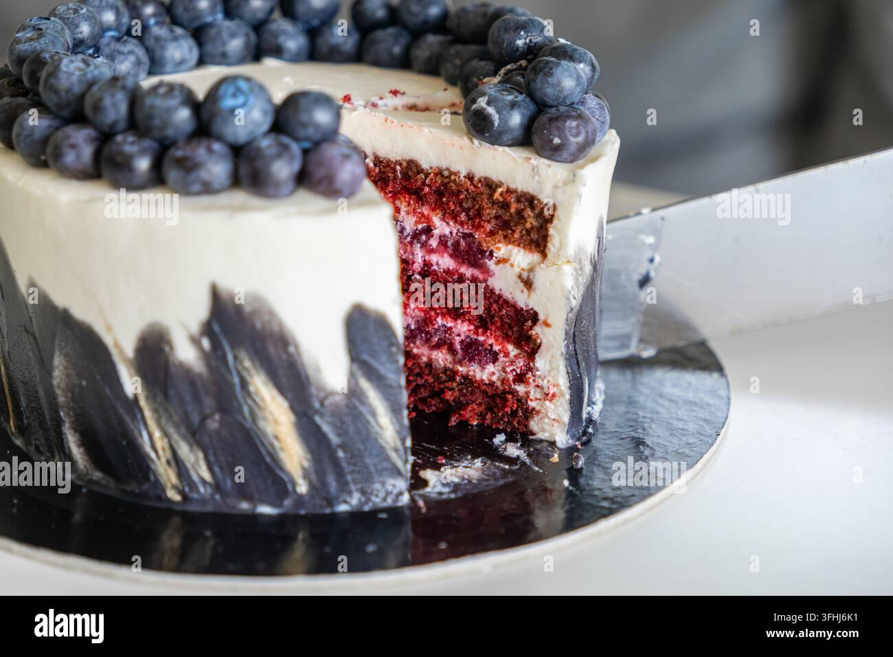 Una torta elegante a strati di velluto rosso con bacche vivaci e glassa liscia aspetta di essere tagliata, presentando un'estetica di panetteria professionale per il lusso Foto Stock