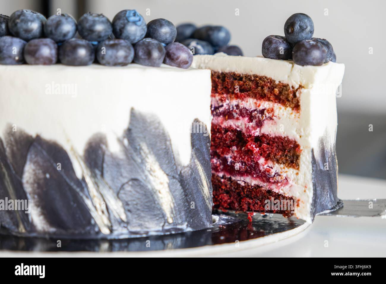Torta a strati di pan di spagna ricoperta di mirtilli freschi e glassa artistica, presentata in uno stile gourmet che riflette una pasticceria di alta qualità e dolci per feste Foto Stock